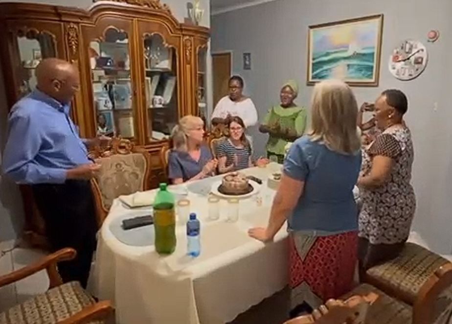 A group of people are standing around a table with a cake on it.