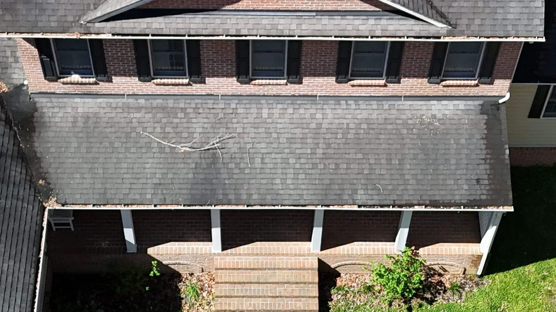 Aerial view of a two-story house with a gray shingled roof and front porch steps.