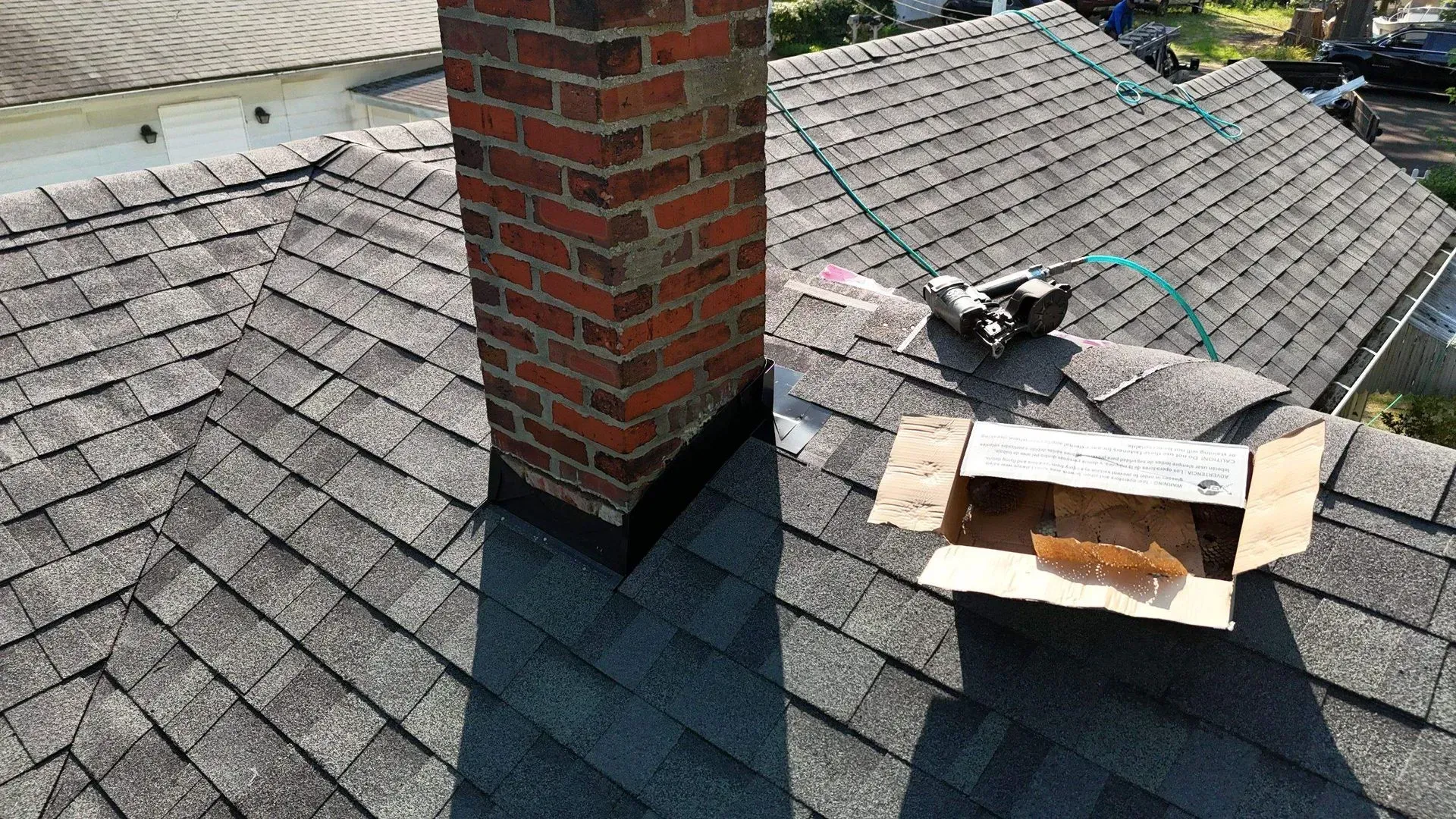 Roof with damaged shingles and a brick chimney; a person is repairing the roof near an open vent.