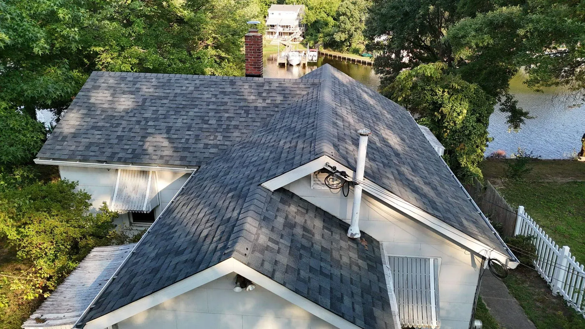 Aerial view of a house with a gray shingle roof beside water and trees.