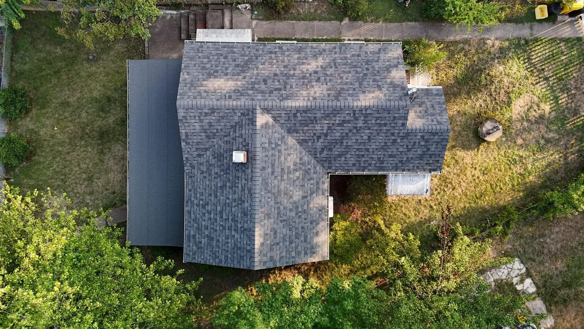 Aerial view of a gray-shingled house roof surrounded by trees and greenery.