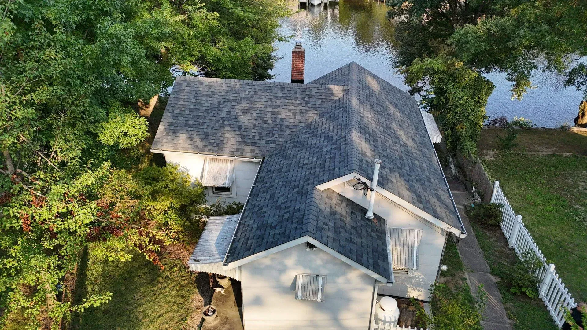 Aerial view of a white house with a gray roof surrounded by trees and water.