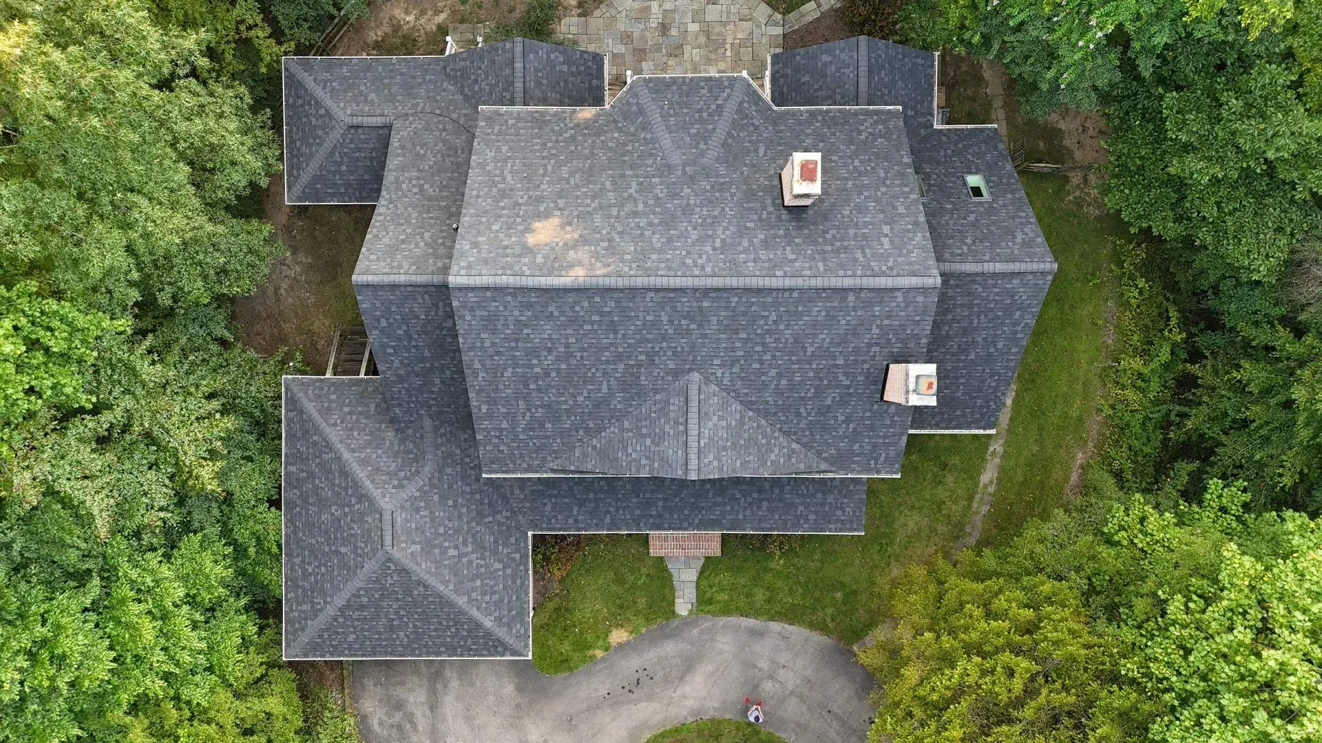 Aerial view of a dark gray house surrounded by dense green trees.
