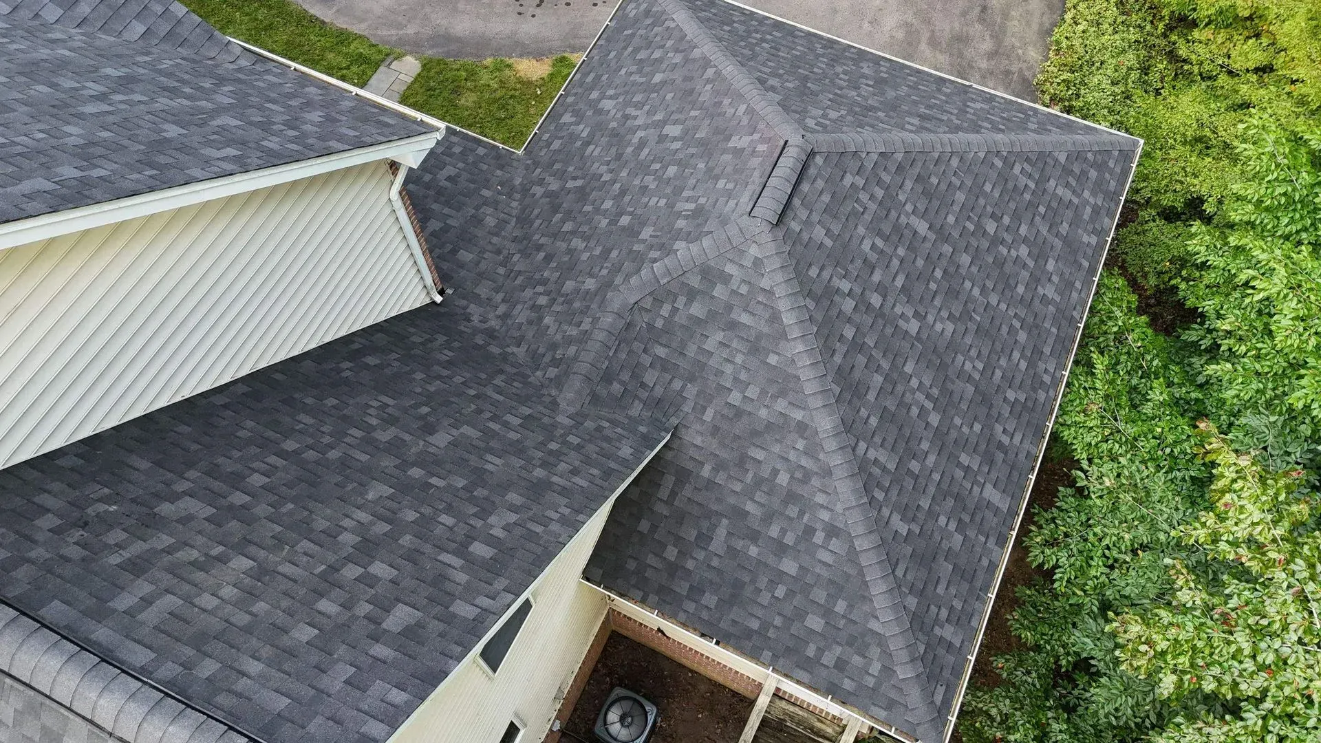 Aerial view of a house roof with dark gray shingles and a small yard nearby.