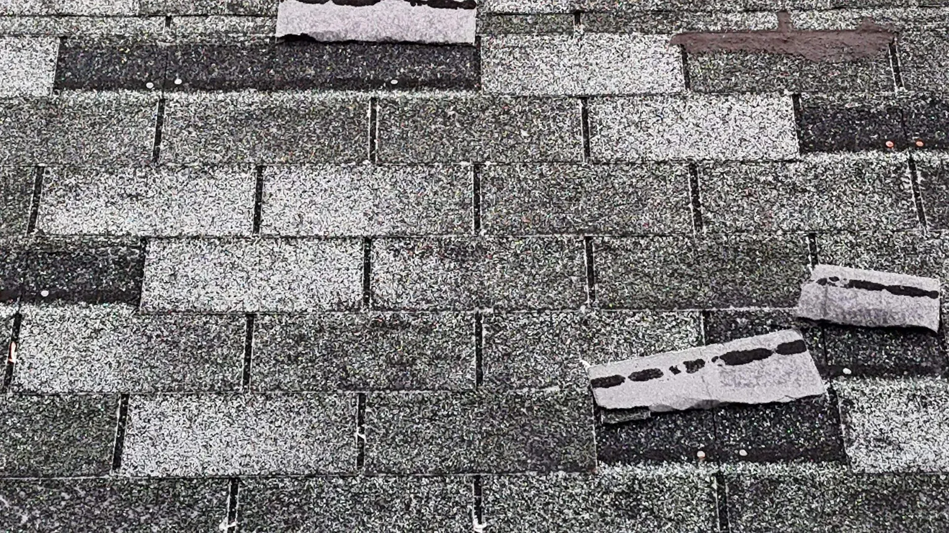 Damaged gray shingle roof with several broken tiles scattered across the surface