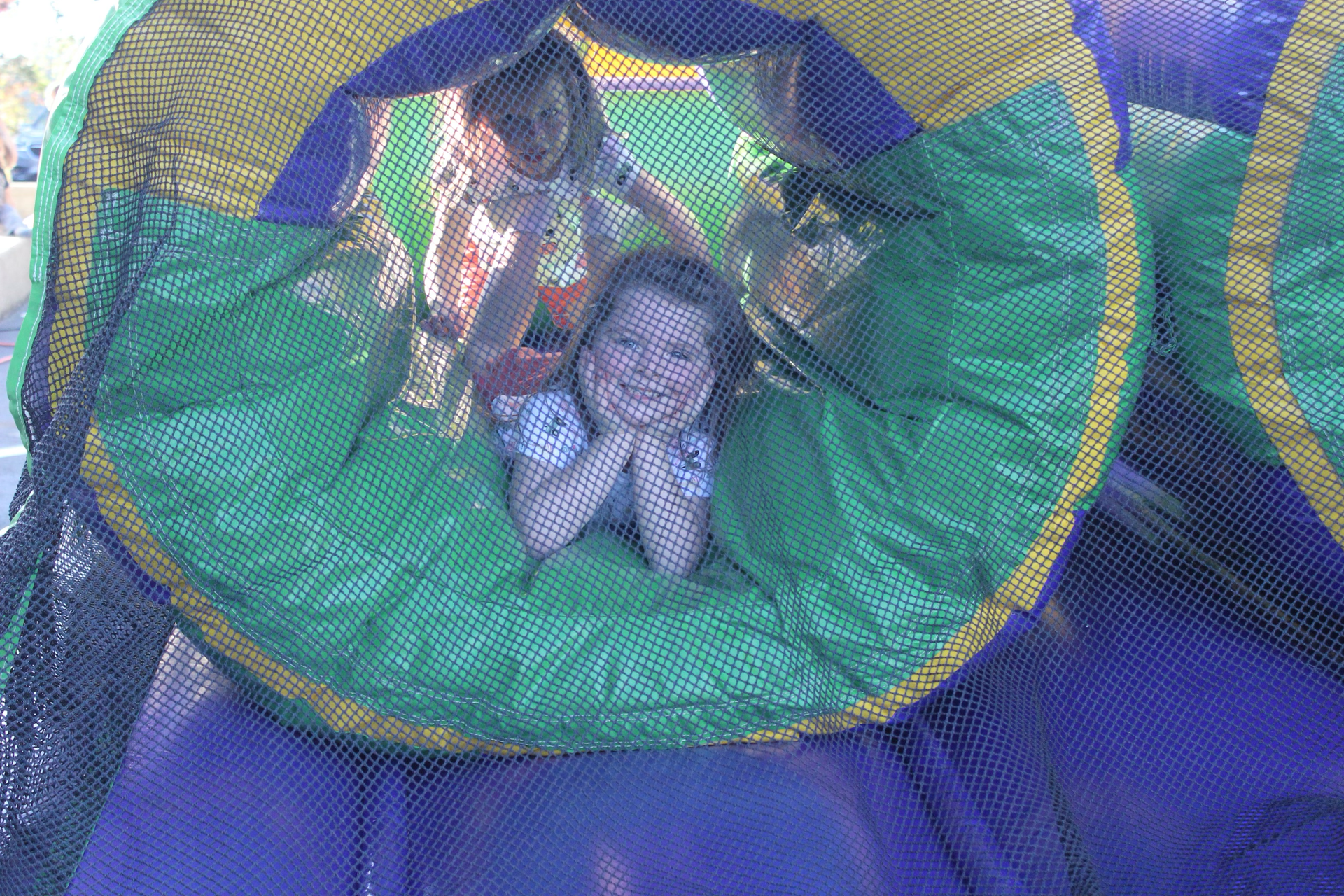 Two children in a colorful inflatable tunnel, one smiling and leaning forward, the other behind.