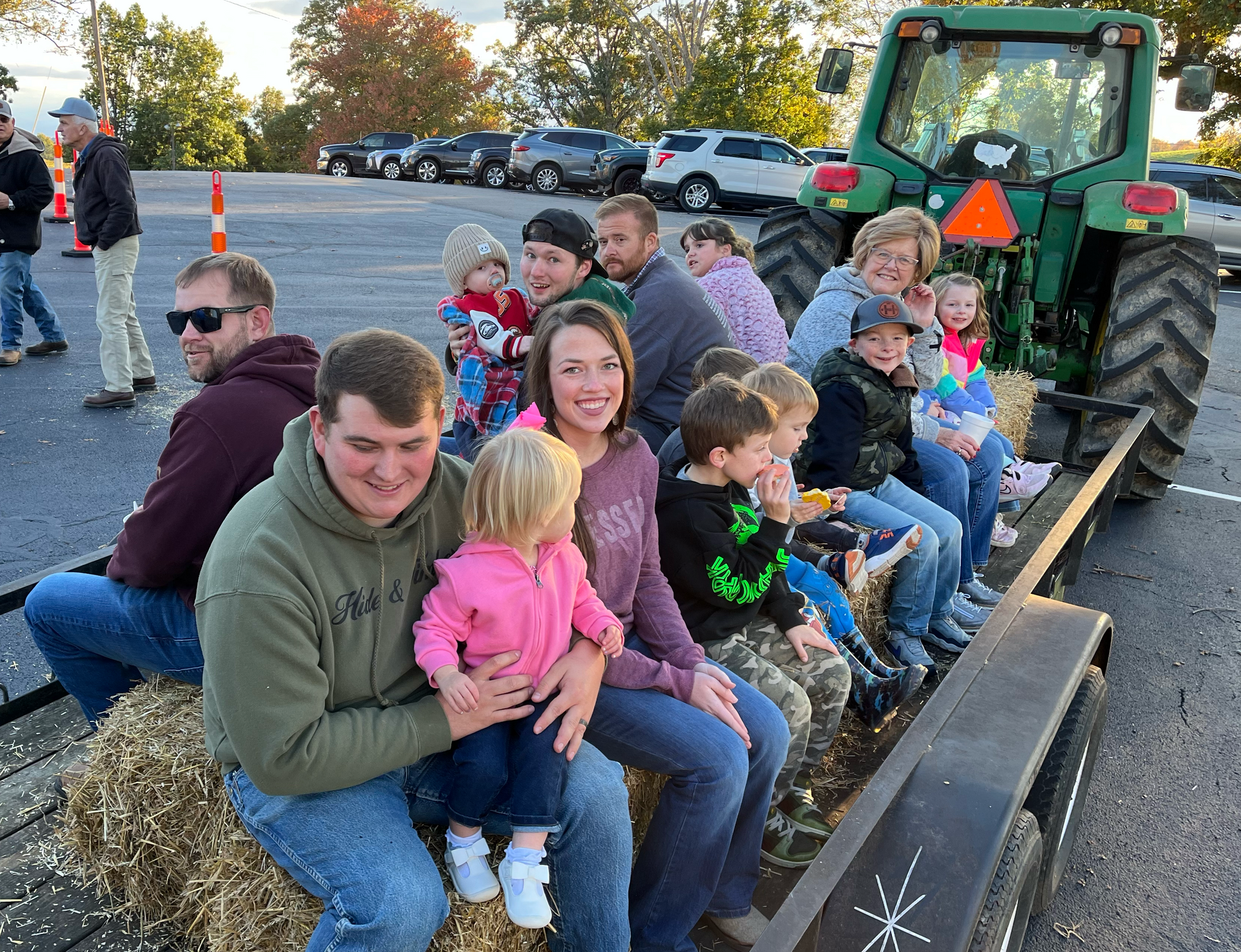 People on a hayride trailer pulled by a green tractor, likely at a fall event.