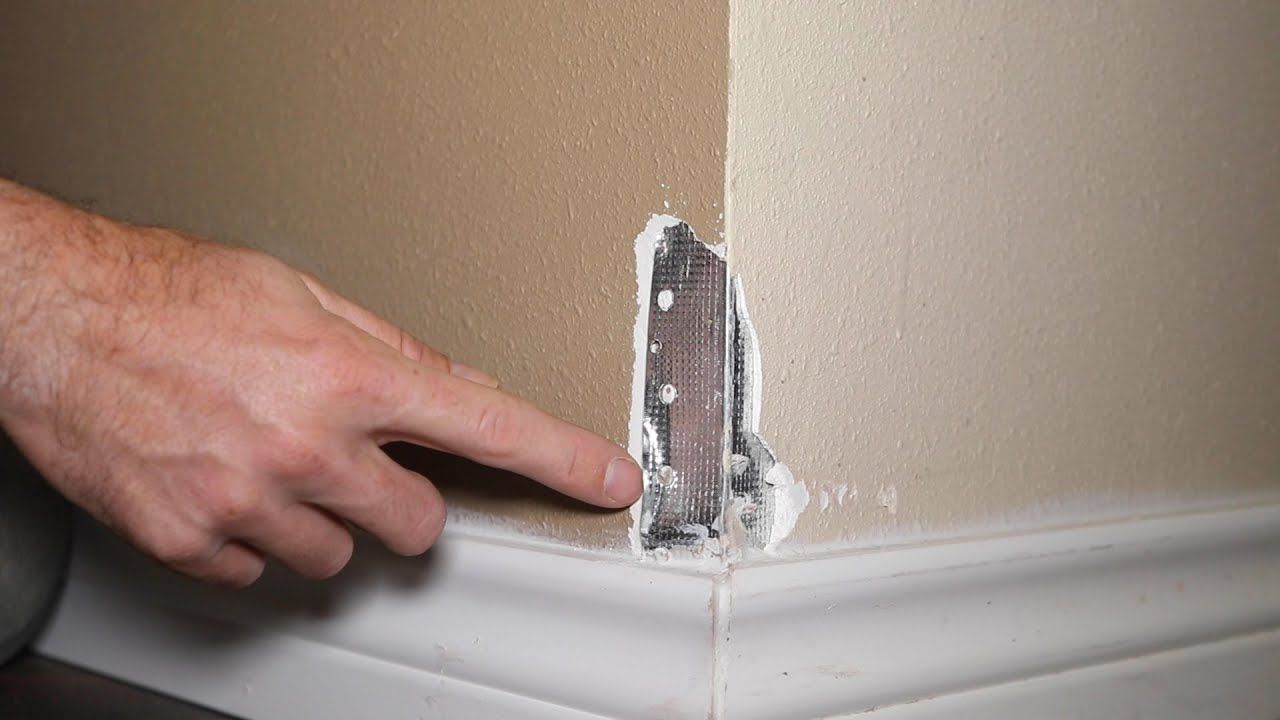 A man is kneeling down while painting a wall with a paint roller.