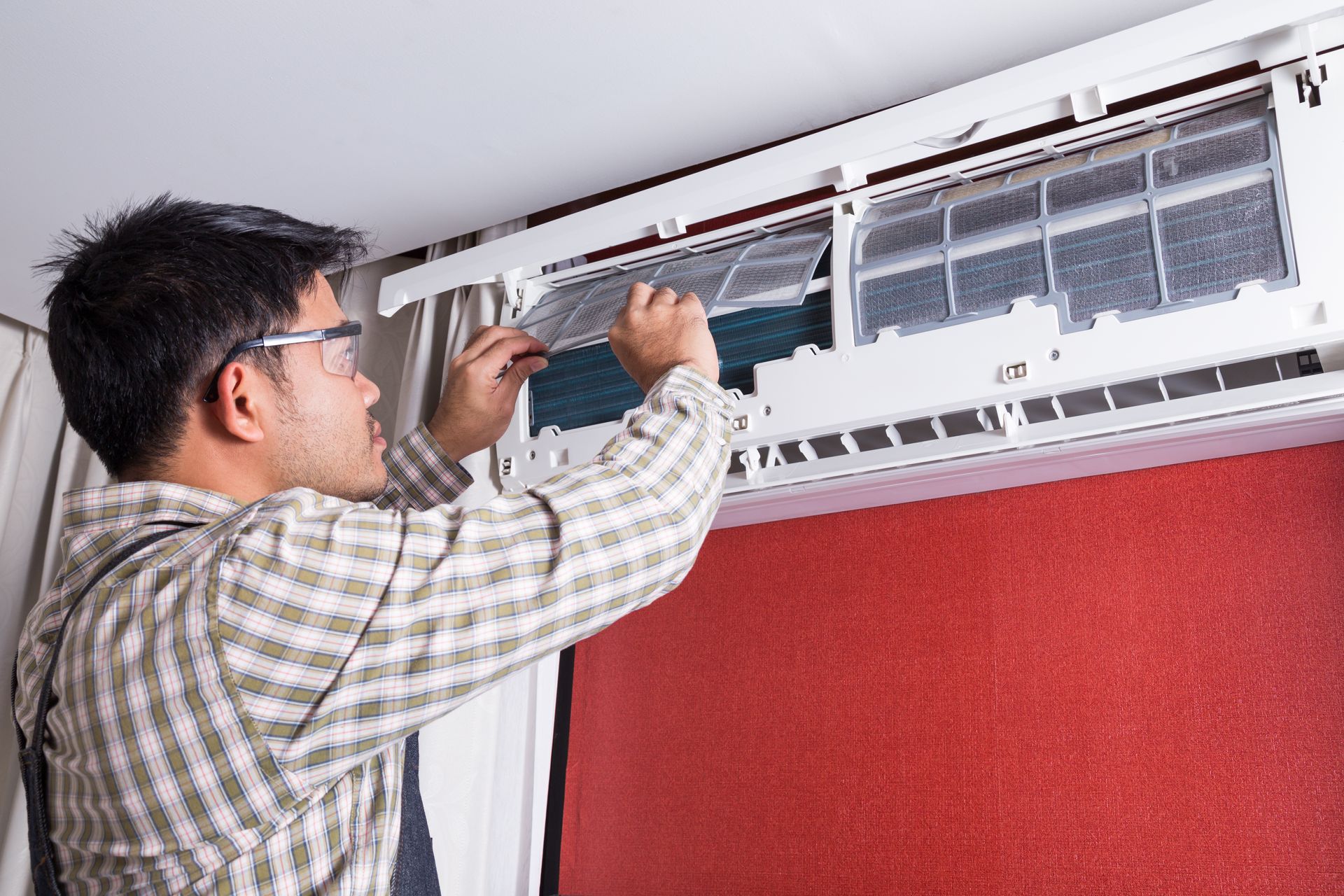 Man cleaning an air conditioner filter indoors, wearing glasses and a plaid shirt. Man cleaning an air conditioner filter indoors, wearing glasses and a plaid shirt.