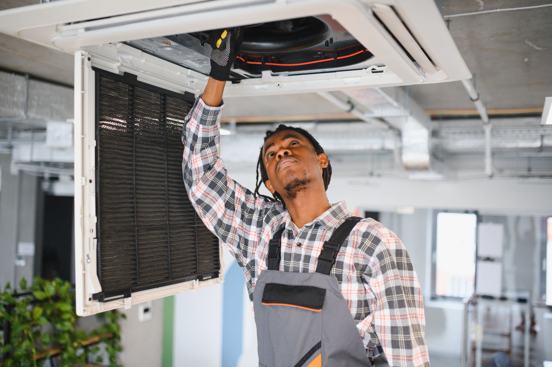 A person in overalls inspects a ceiling air conditioning unit. A person in overalls inspects a ceiling air conditioning unit.