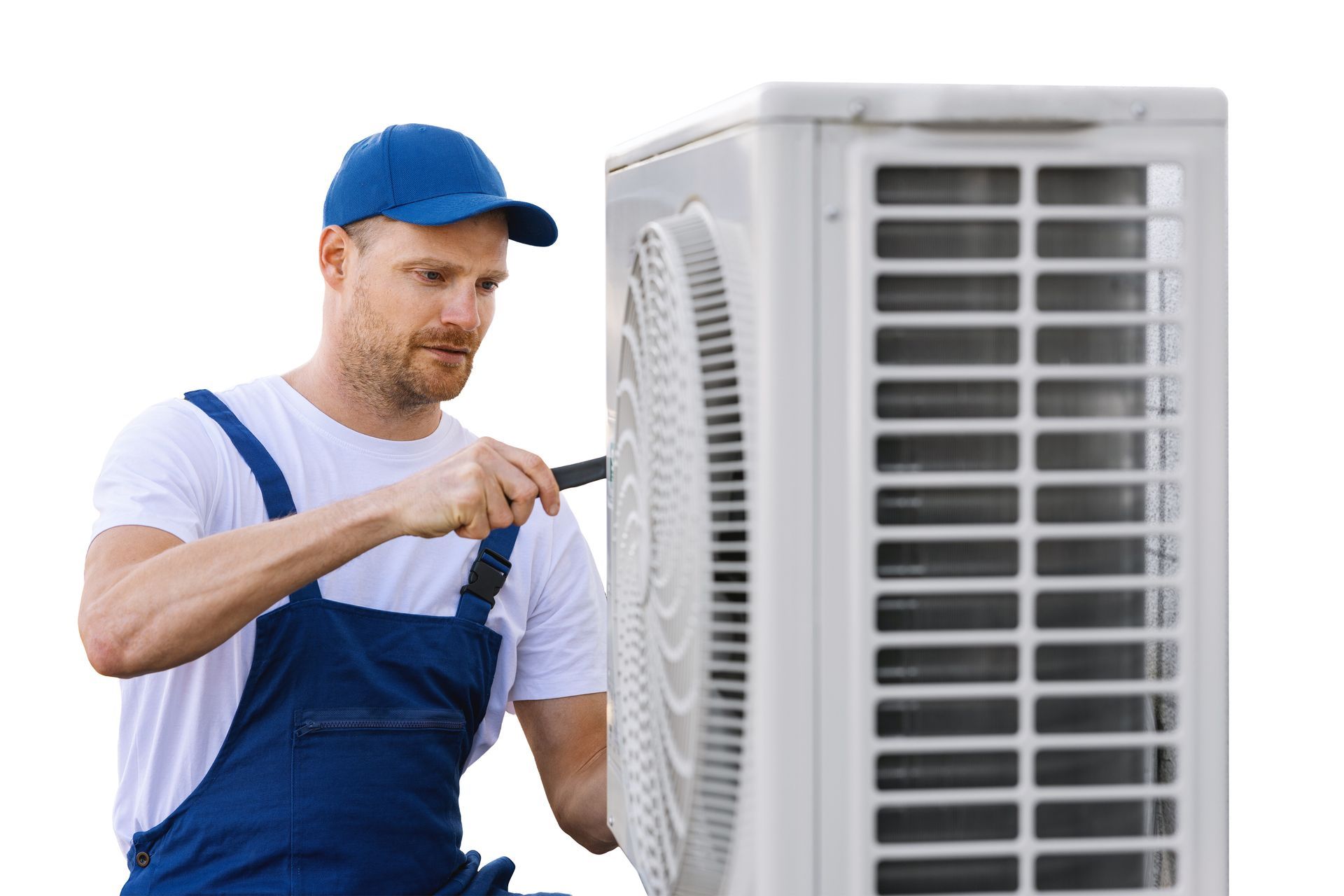 A technician in blue overalls is repairing an outdoor AC unit with a screwdriver