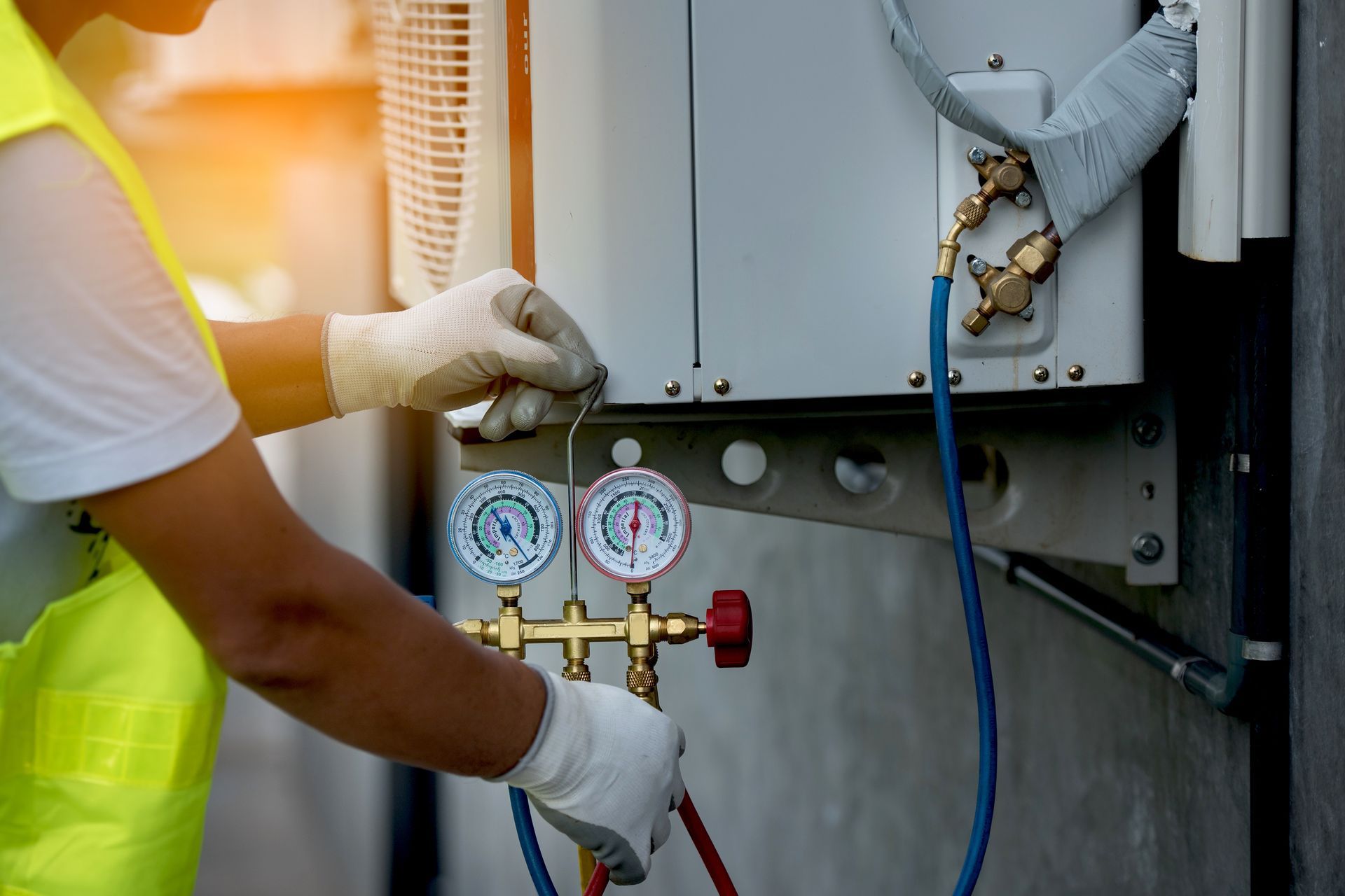 HVAC technician in gloves connecting gauges to an AC unit outside. HVAC technician in gloves connecting gauges to an AC unit outside.