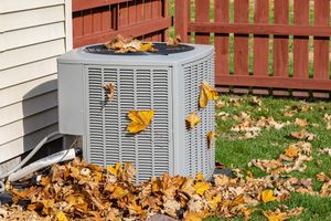AC unit covered in fall leaves next to a wooden fence.