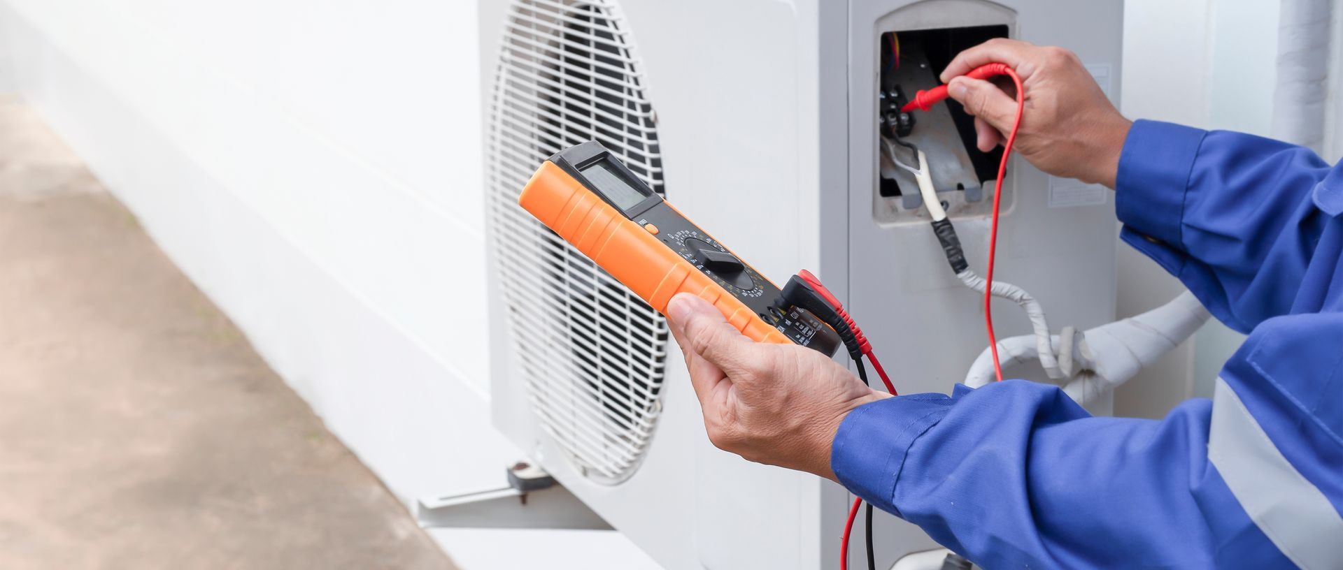 Technician using a digital multimeter to test an outdoor air conditioning unit