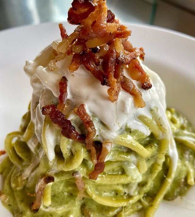 Piatto di pasta con salsa verde, guarnito con besciamella cremosa e pancetta croccante.