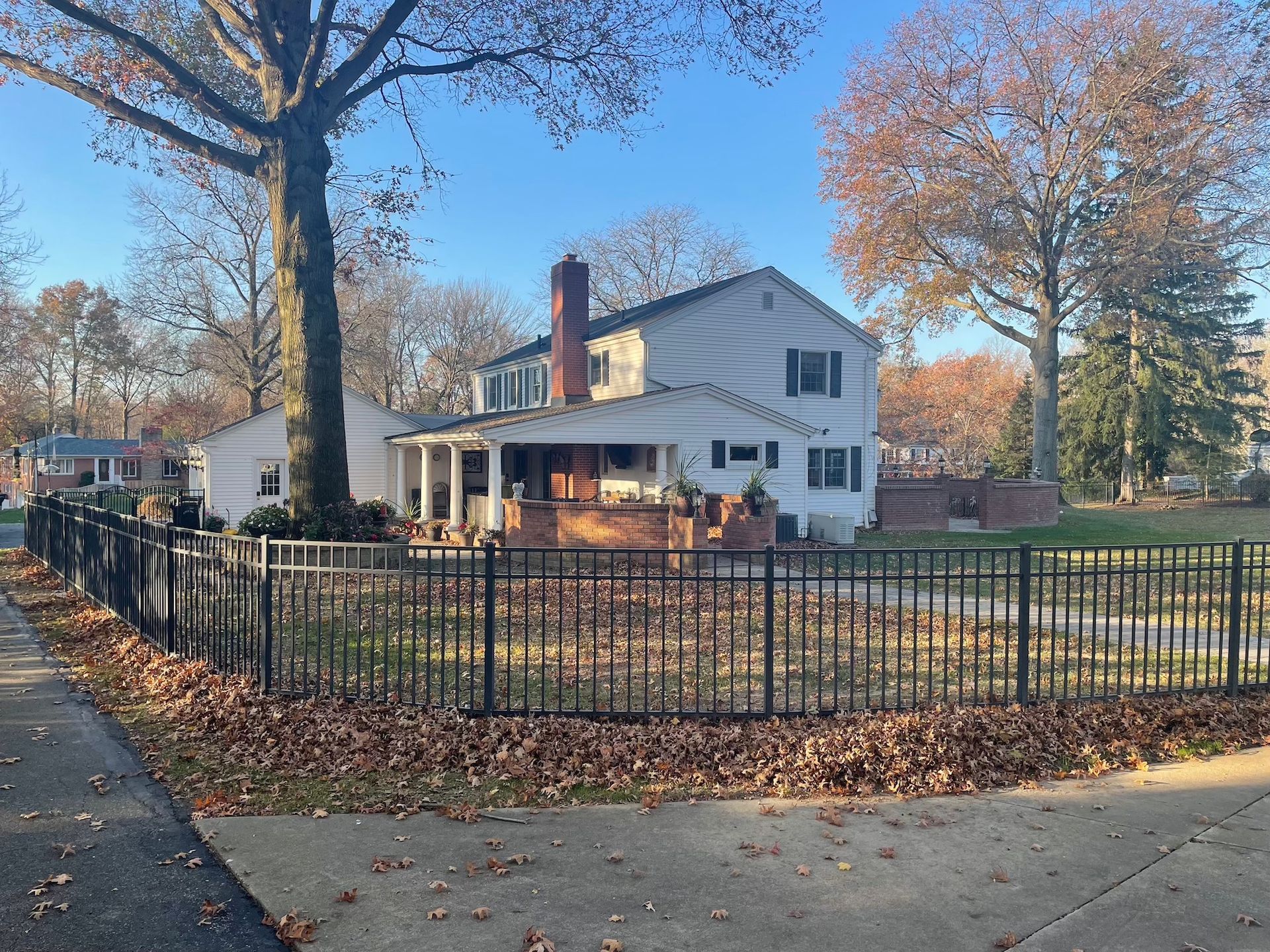 A house with a fence around it and a lot of leaves on the sidewalk.