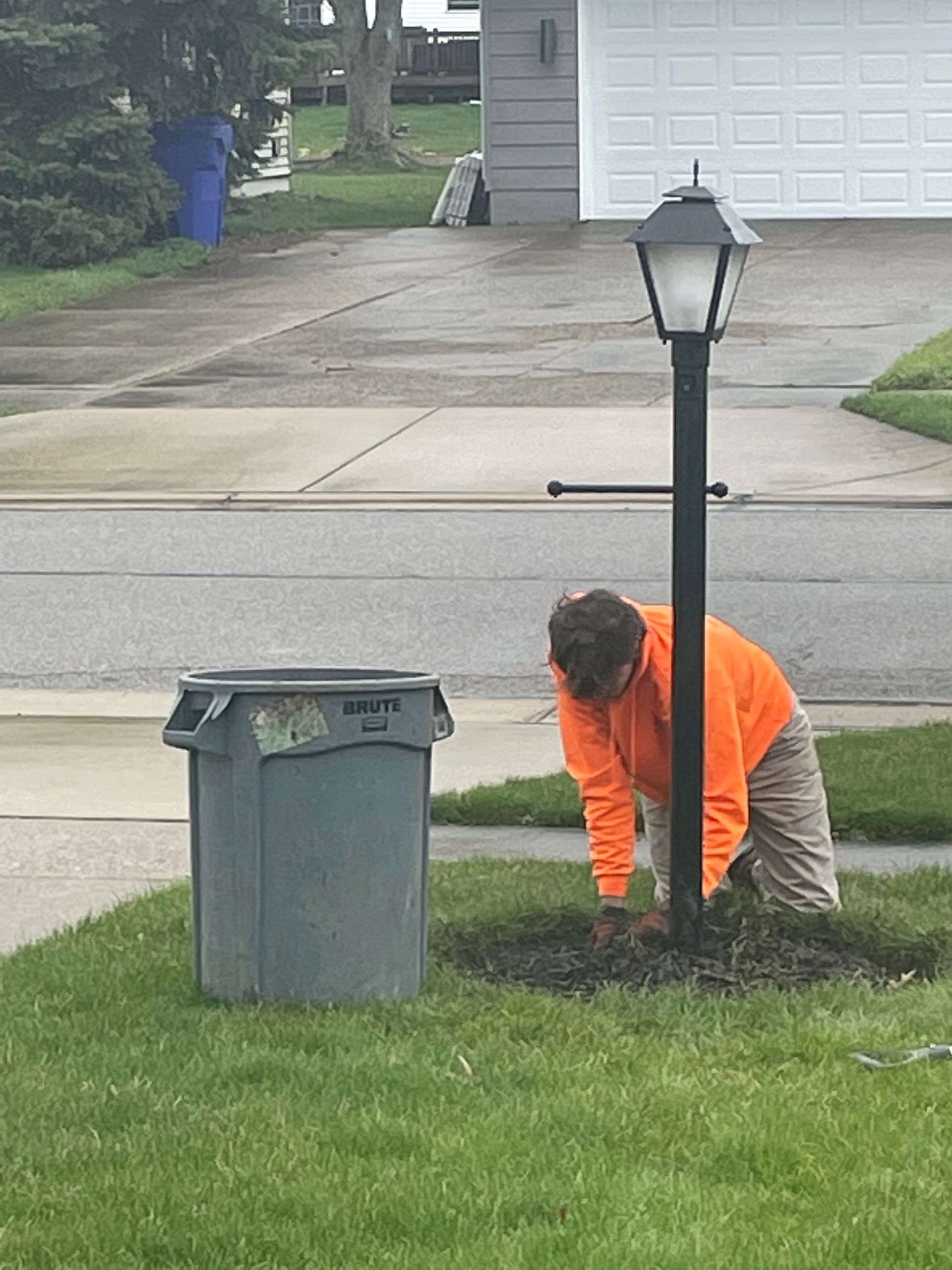 A man is kneeling down next to a lamp post and a trash can.