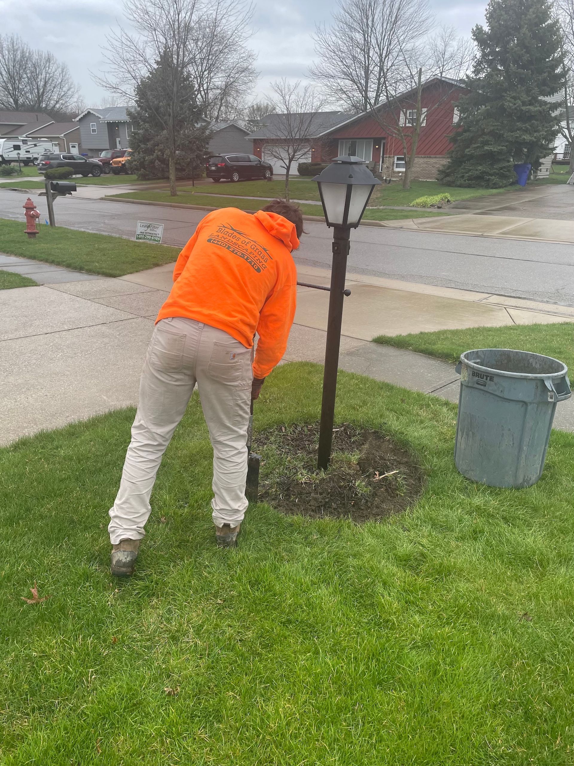 A man in an orange hoodie is standing in the grass next to a lamp post.