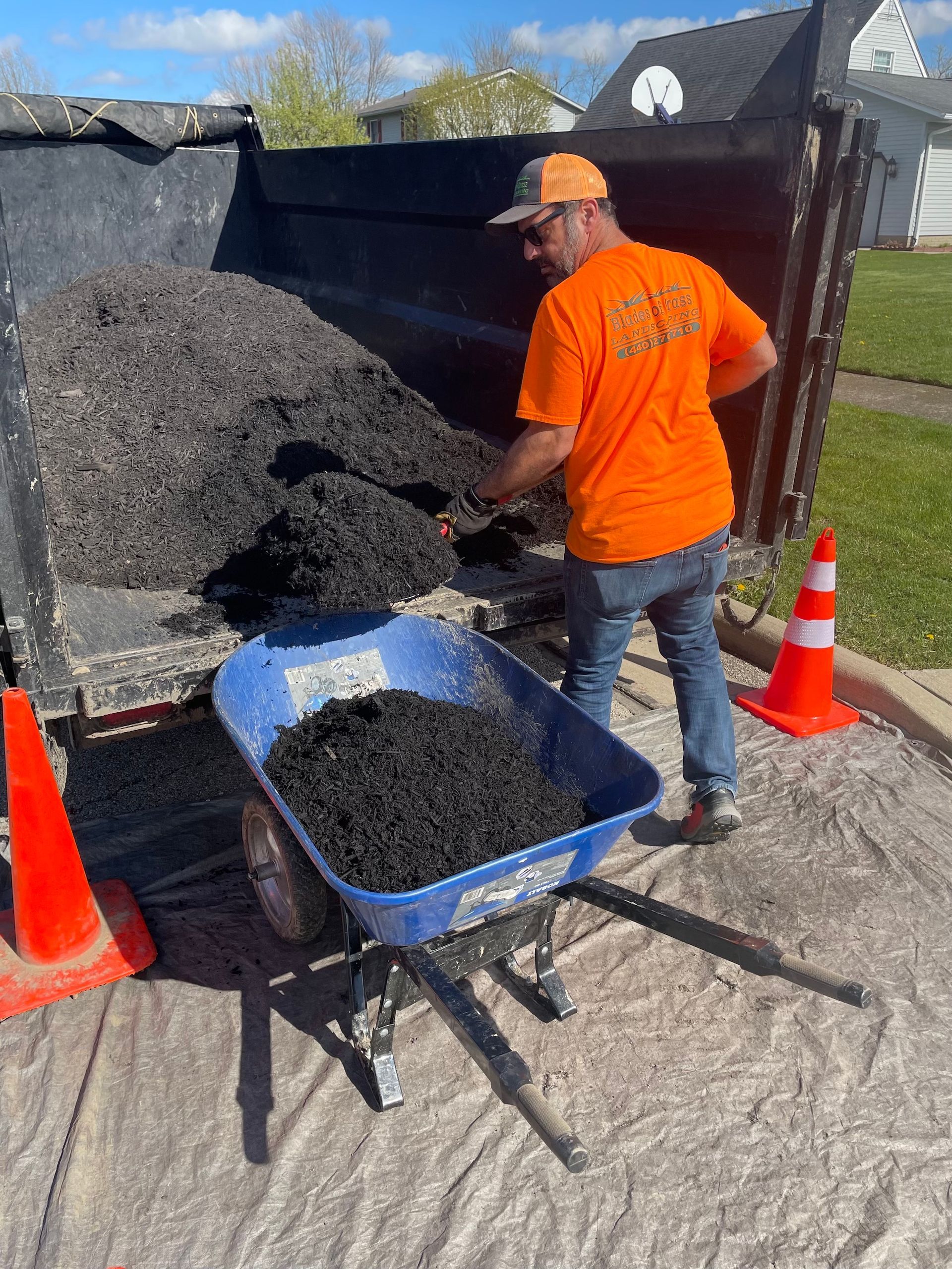 A man is loading a wheelbarrow full of dirt into a dumpster.