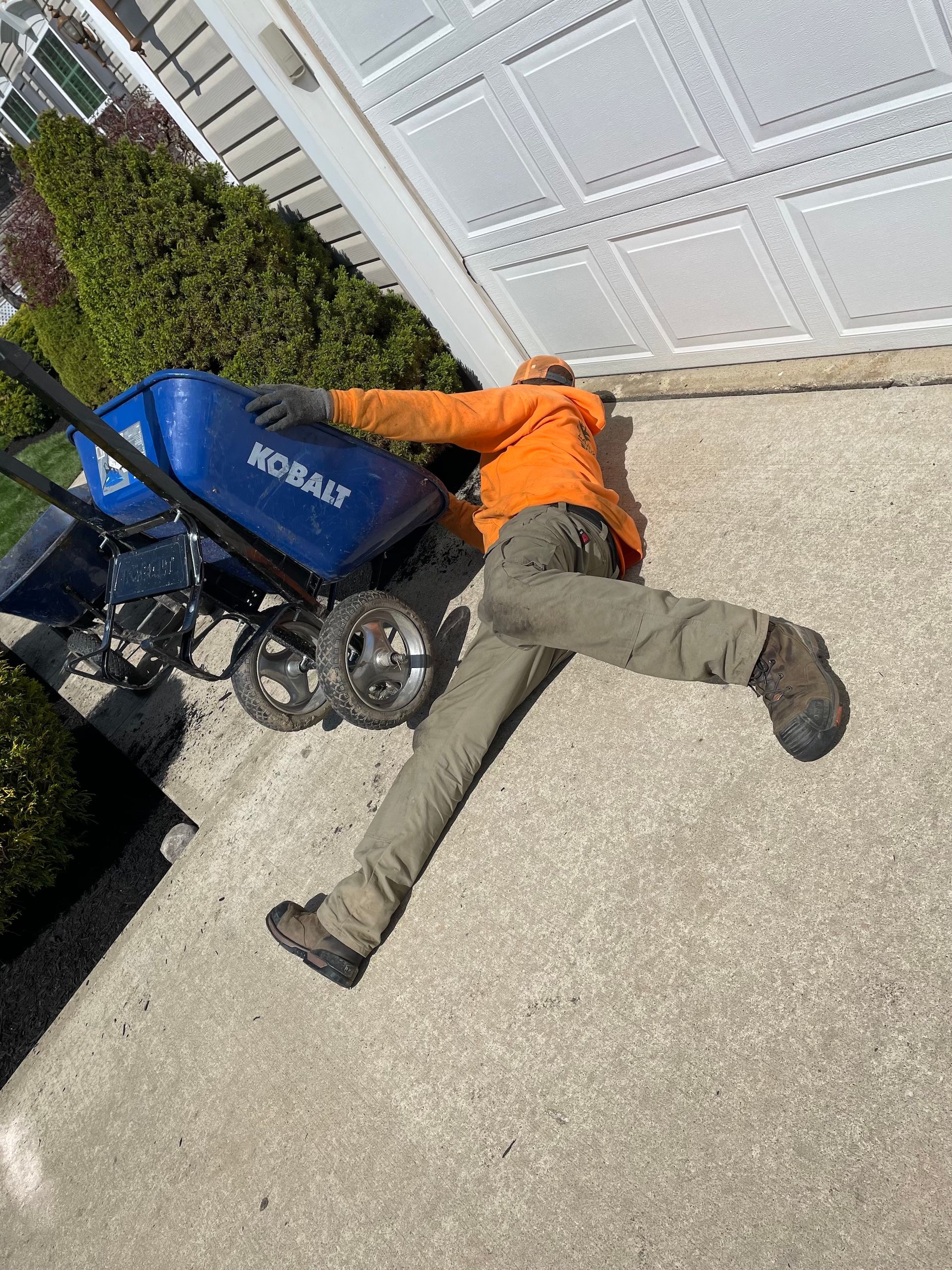 A man is laying on the ground next to a wheelbarrow.