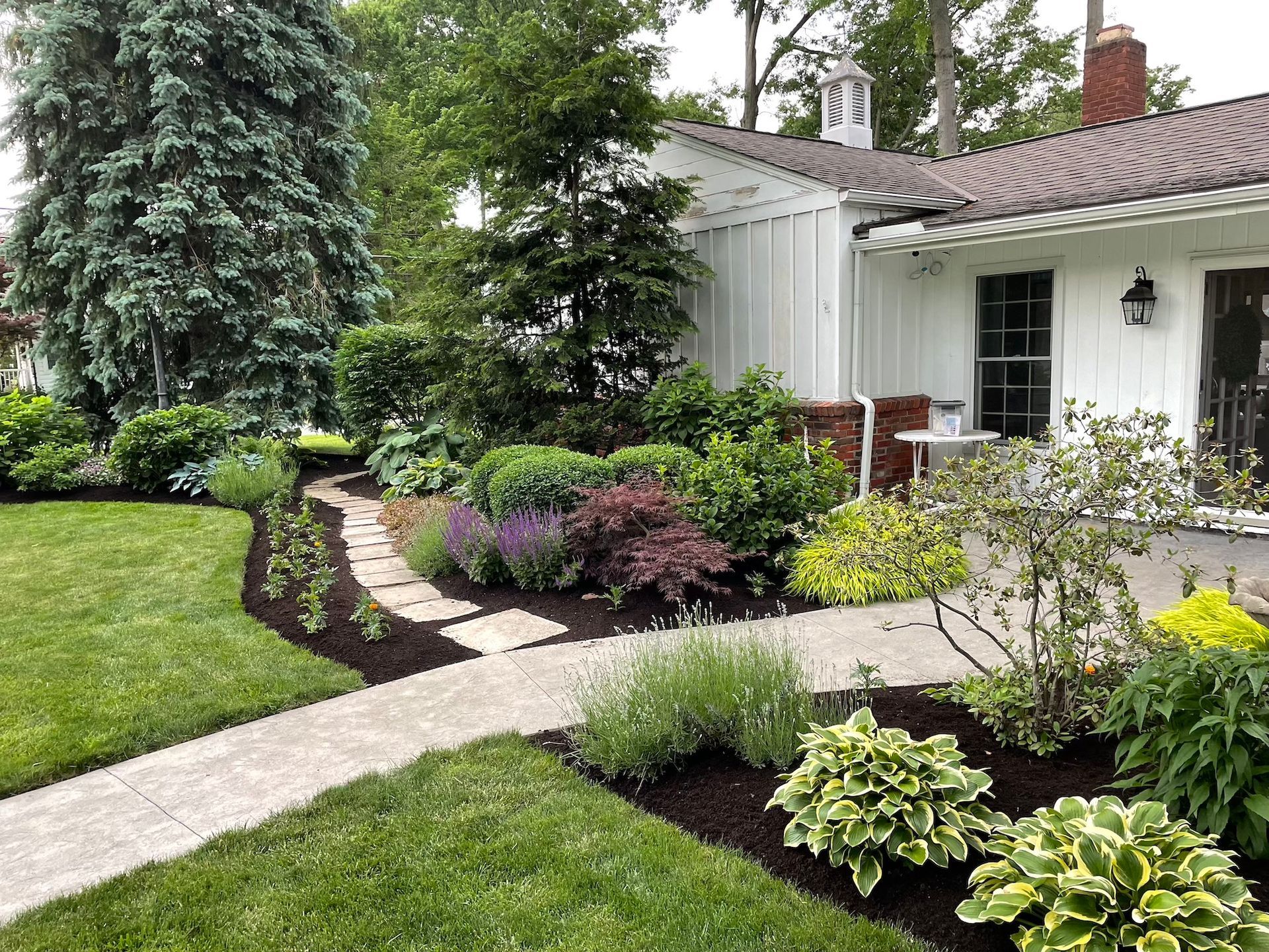 A white house with a lush green lawn and a walkway leading to it.