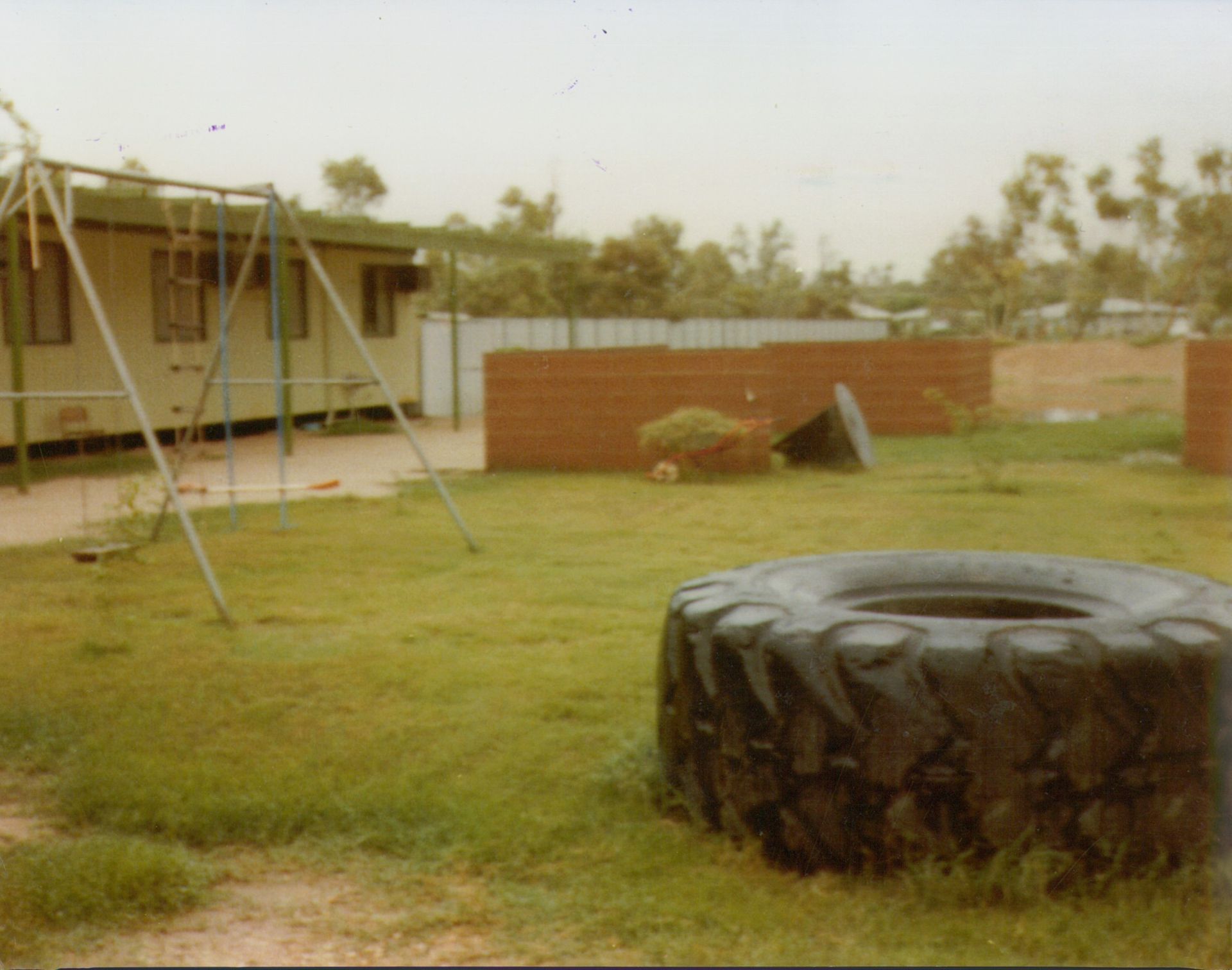 A playground with a tire swing, a large stationary tire in the grass, and a modular building in the background.