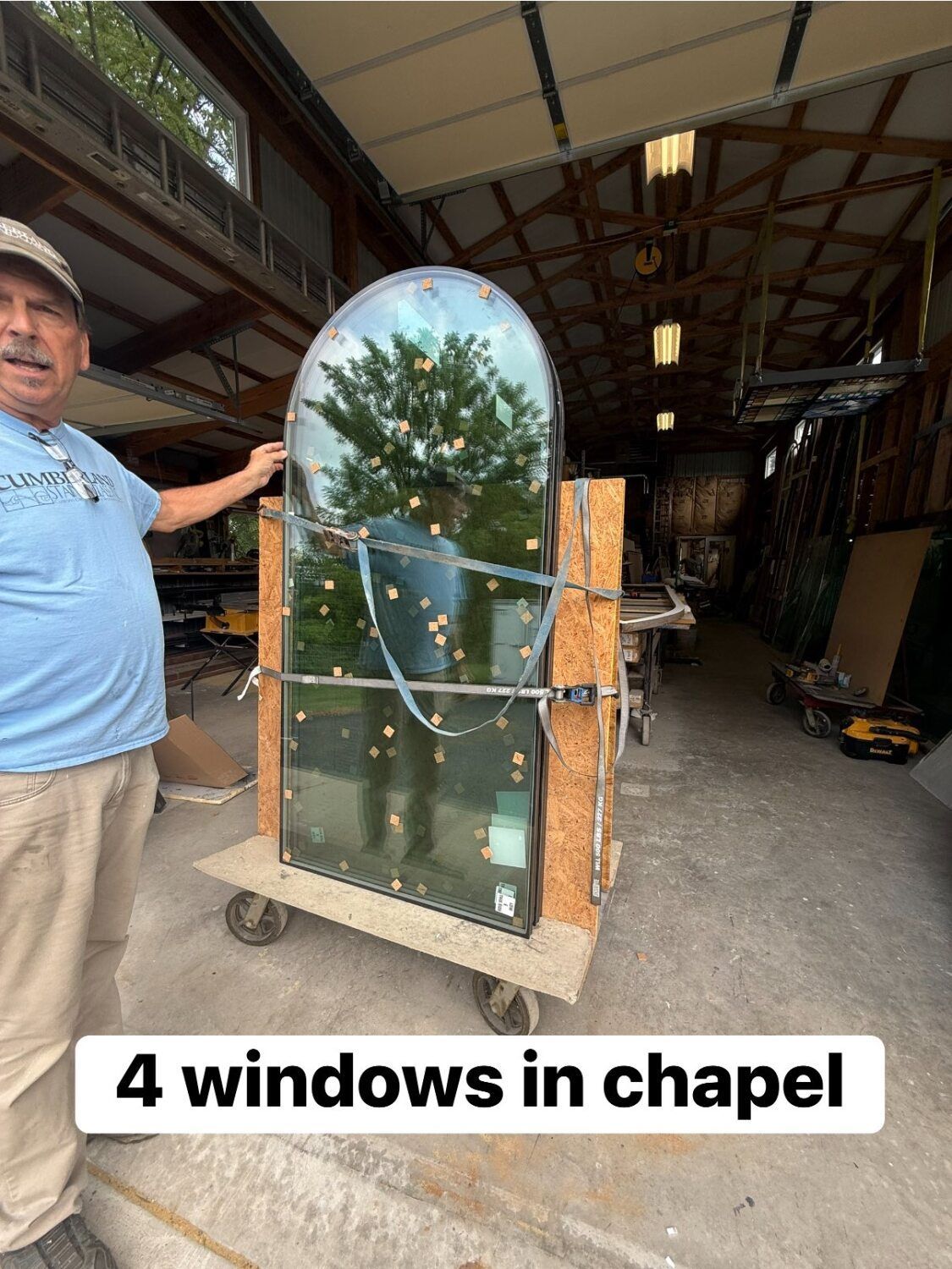 Man stands next to a large window on a wheeled platform, inside a building.