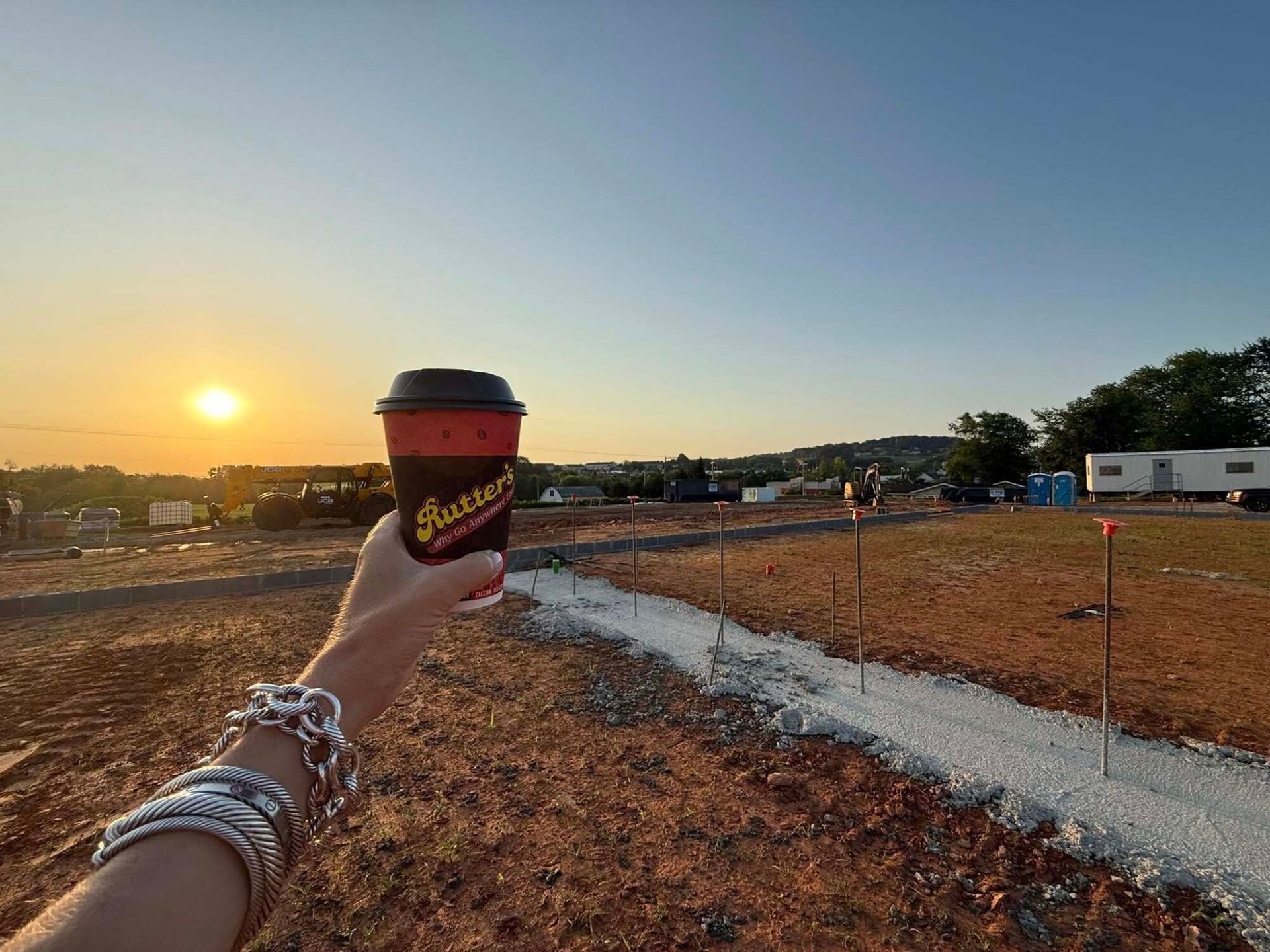Hand holding a coffee cup at sunset, overlooking an active construction project site