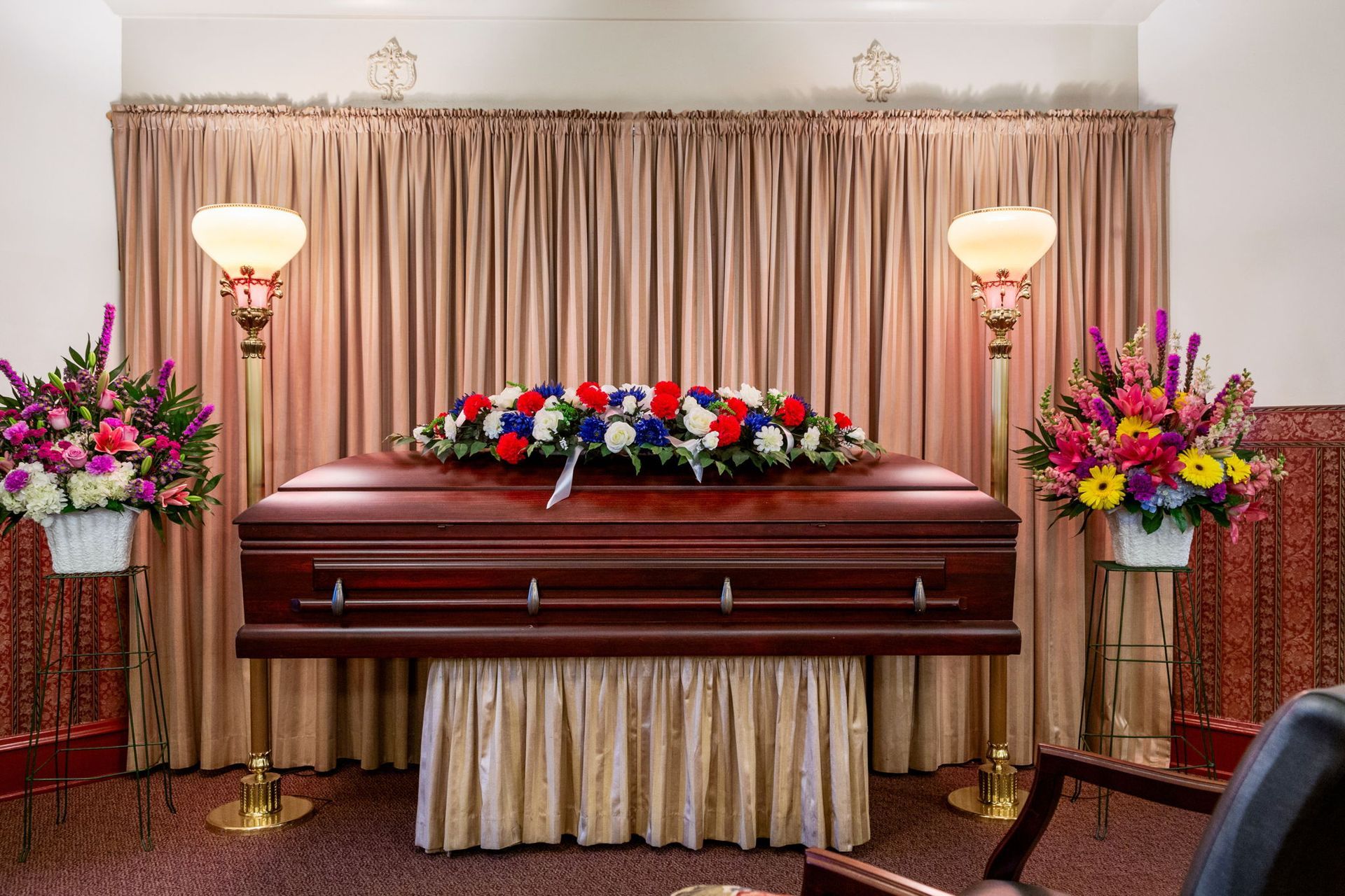A closed, brown casket with floral arrangements in a funeral home setting.