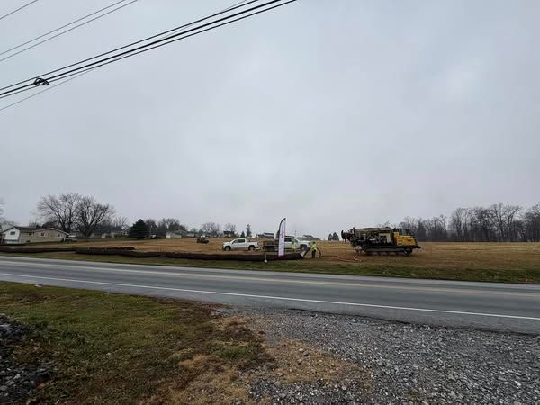 A gray, overcast day shows a road with a truck and construction equipment on a grassy field.