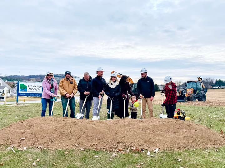 Group of people at a groundbreaking ceremony, shovels in the dirt, cloudy day.