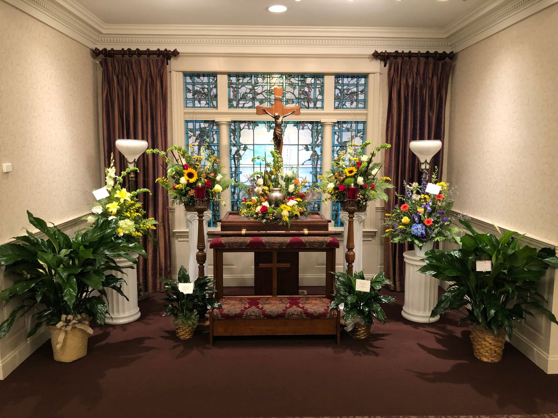 A group of people is gathered around an urn surrounded by red roses at a memorial service