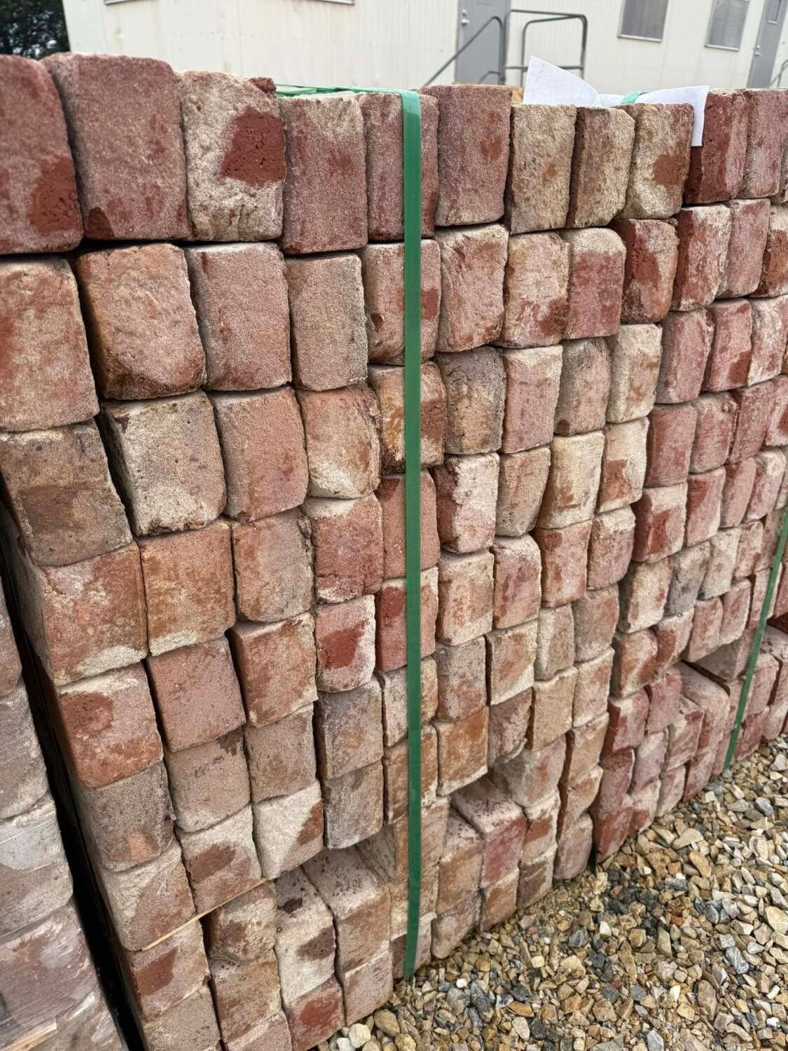 Stack of weathered, reddish-brown bricks bound with green straps, outdoors.