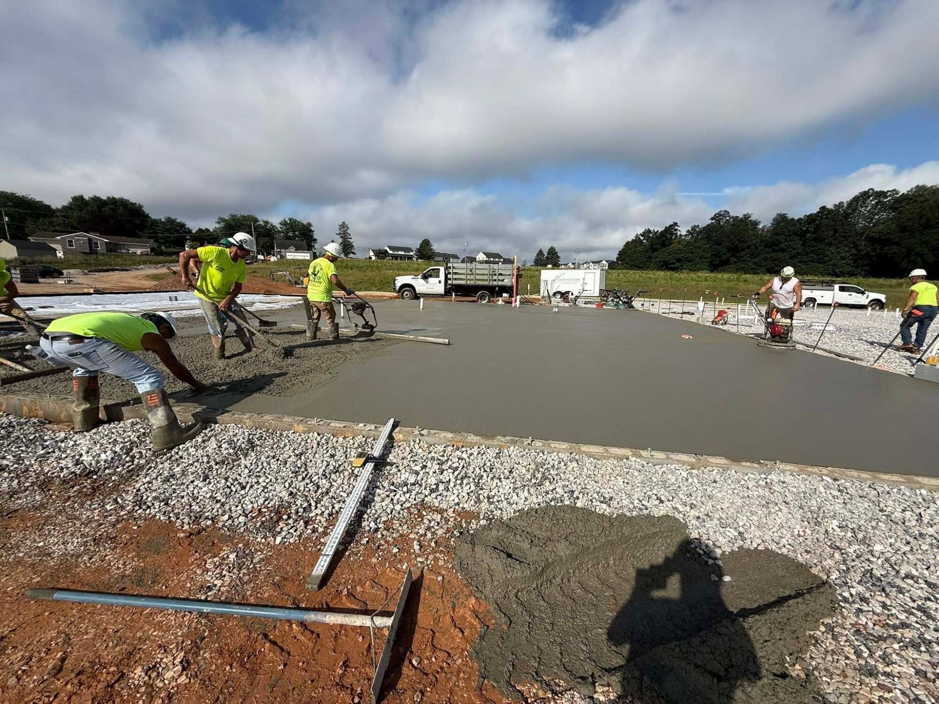 Construction workers smoothing wet concrete on a large, outdoor surface. Cloudy sky.