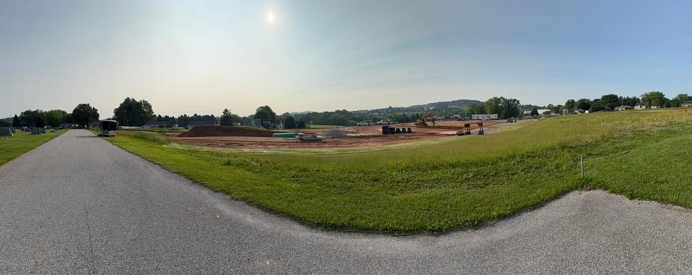 Gravel road leading past a grassy field toward an active construction development site