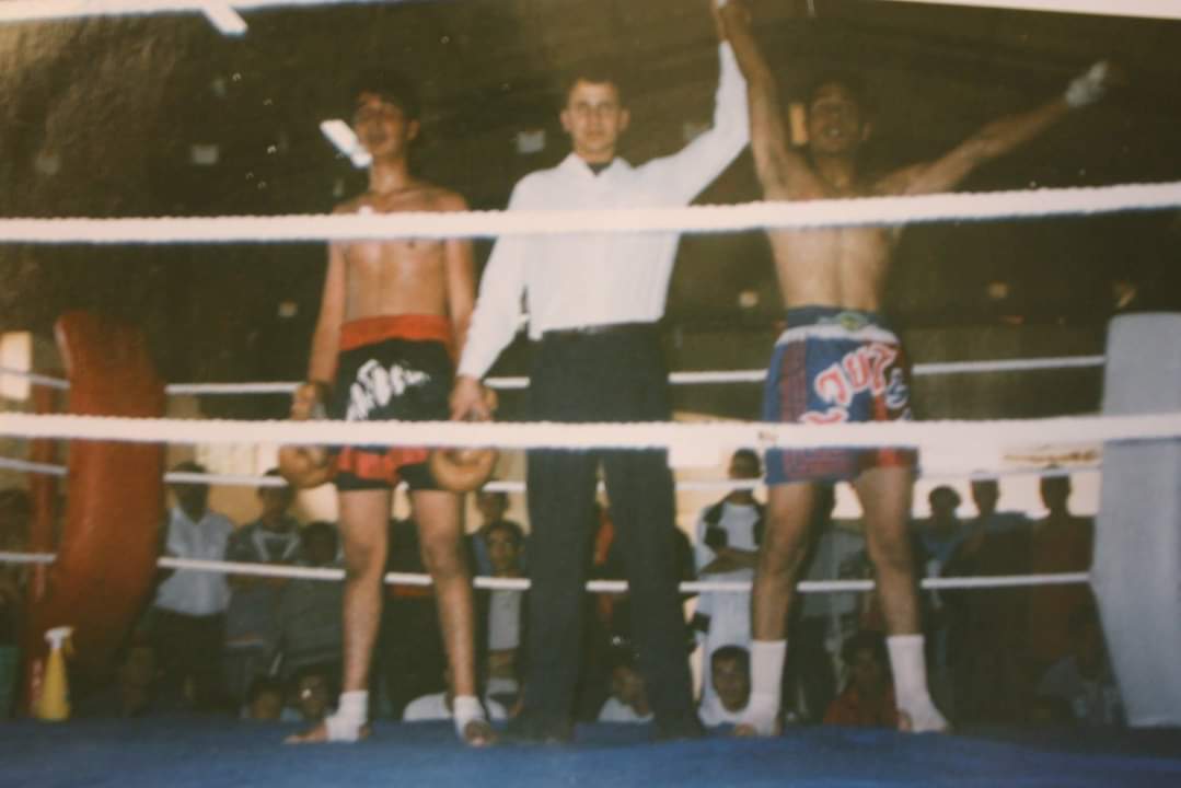 Un ring de boxe avec deux boxeurs et un arbitre debout entre eux, les bras levés pour annoncer le match.