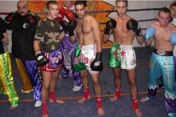 Cinq boxeurs posent sur un ring, portant des gants et des shorts colorés après un combat.