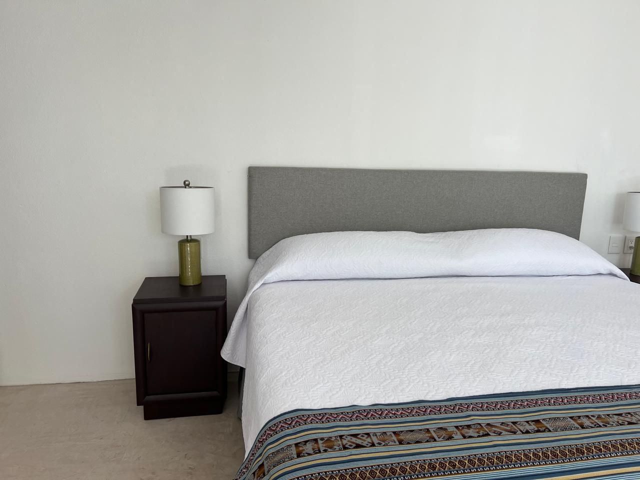 Dormitorio con cama, sofá, dos mesitas de noche, lámparas y ventana con contraventanas.