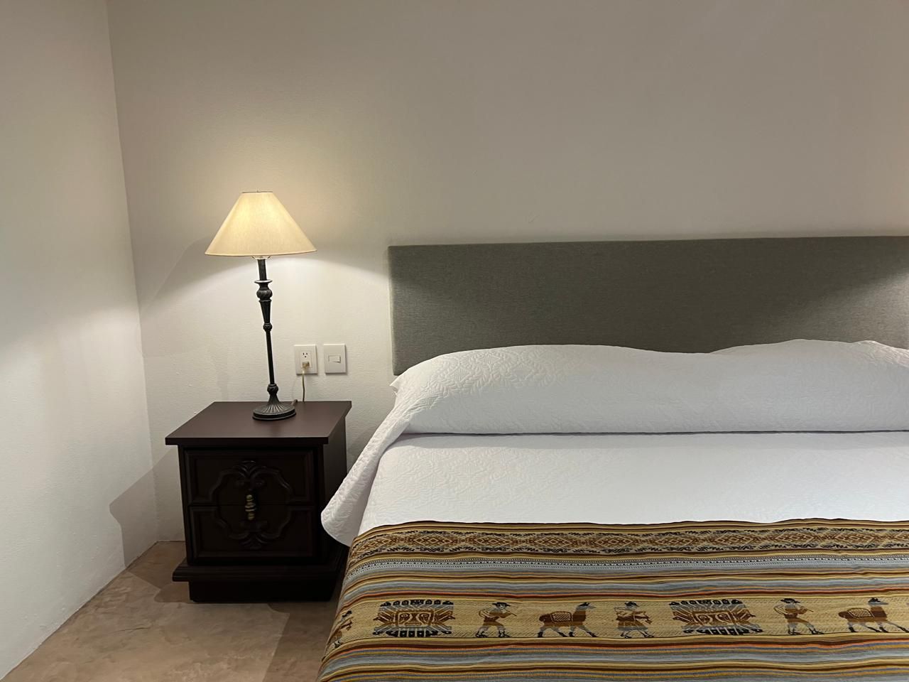 Césped verde bordeado por un muro de piedra, árboles y exuberante follaje, con un edificio en tono rosa al fondo.