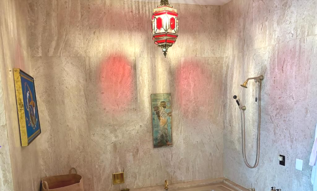 Baño con paredes rosadas, bañera incorporada y una lámpara ornamentada en tonos rojos y blancos.