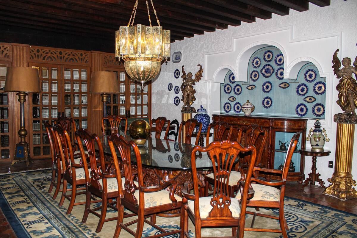 Elegante comedor con mesa grande, sillas ornamentadas, lámpara de araña y pared decorativa.