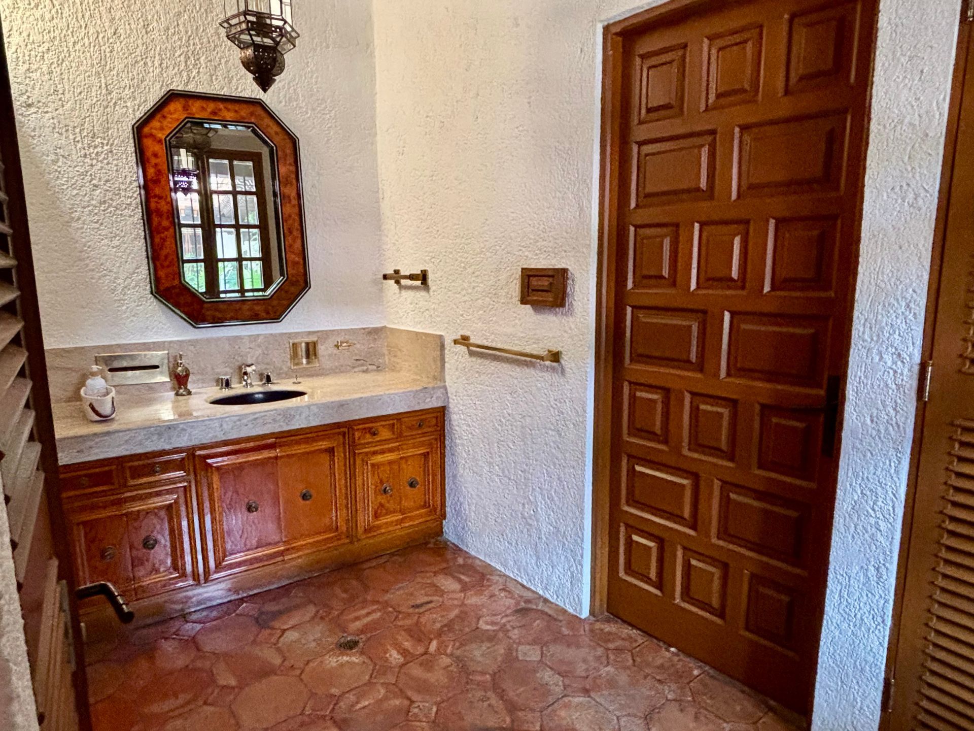 Baño con puerta marrón, tocador con espejo y paredes y piso texturizados.