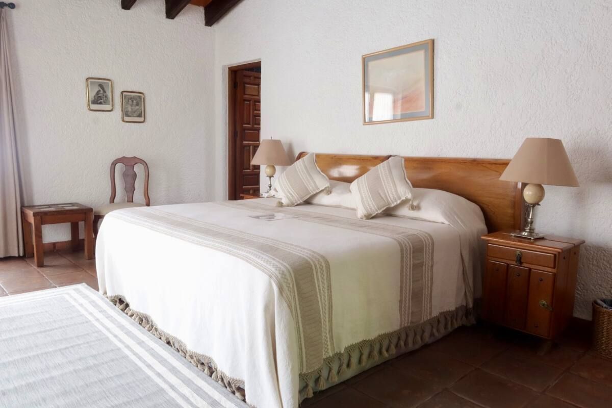 Dormitorio con cama grande, muebles de madera y cuadros. Colores vivos y neutros.