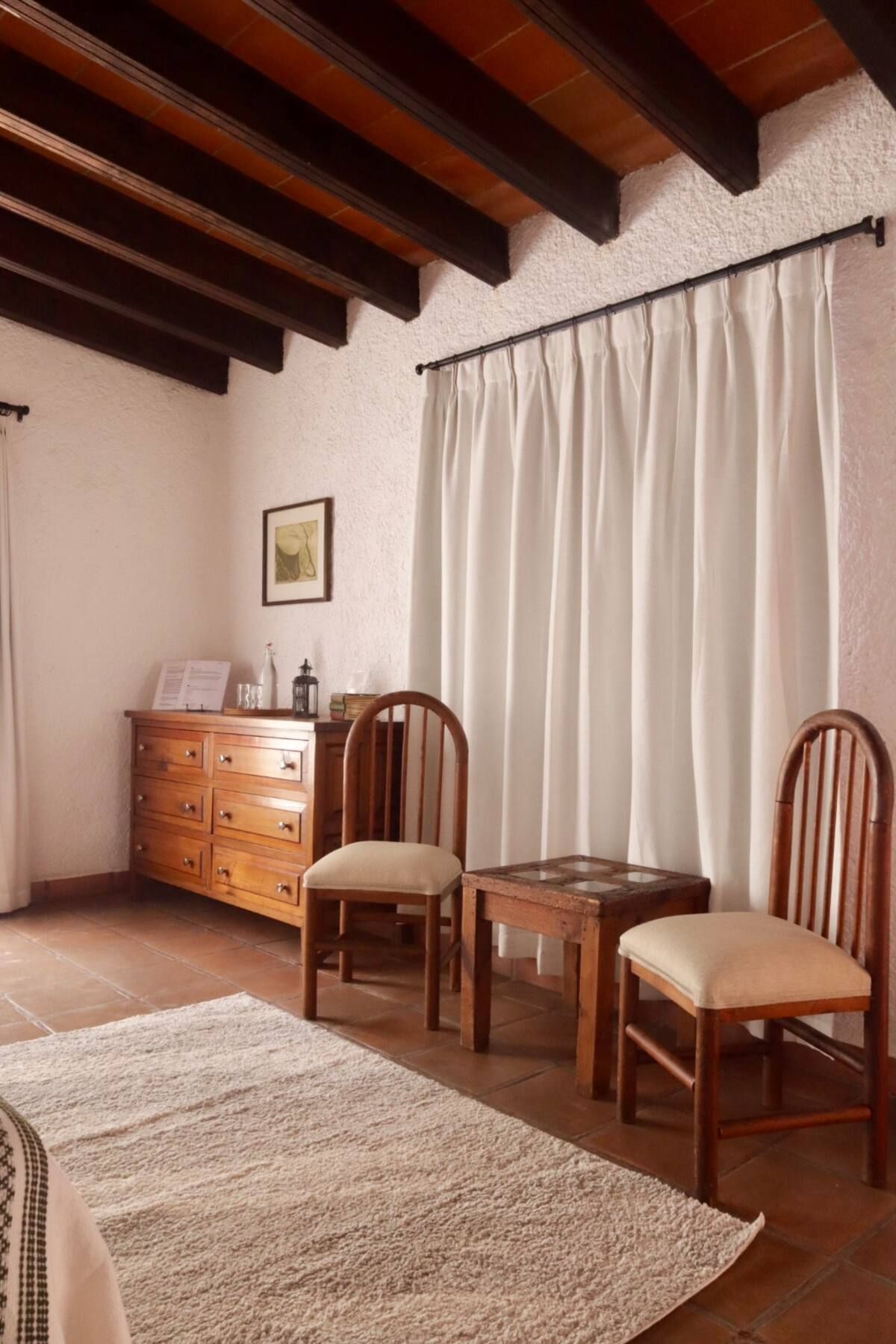 Dormitorio con muebles de madera, cortinas color crema y alfombra texturizada.
