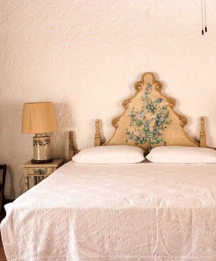 Dormitorio con cabecero floral adornado, lámpara y ropa de cama blanca.