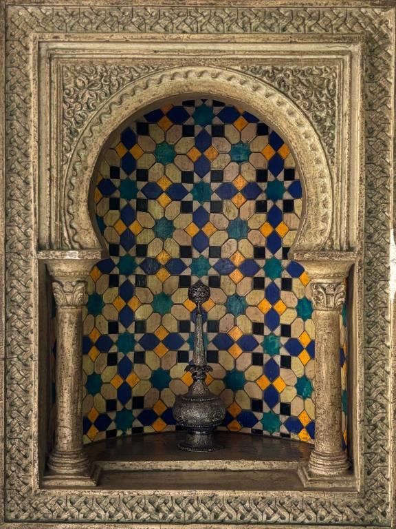 Alcoba arqueada decorativa con mosaico de azulejos y fuente plateada ornamentada.