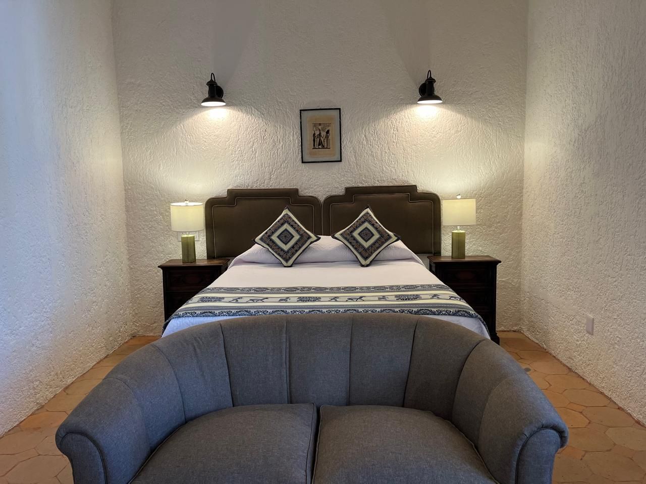 Dormitorio con cama de matrimonio, pequeño sofá, mesitas de noche y apliques de pared.