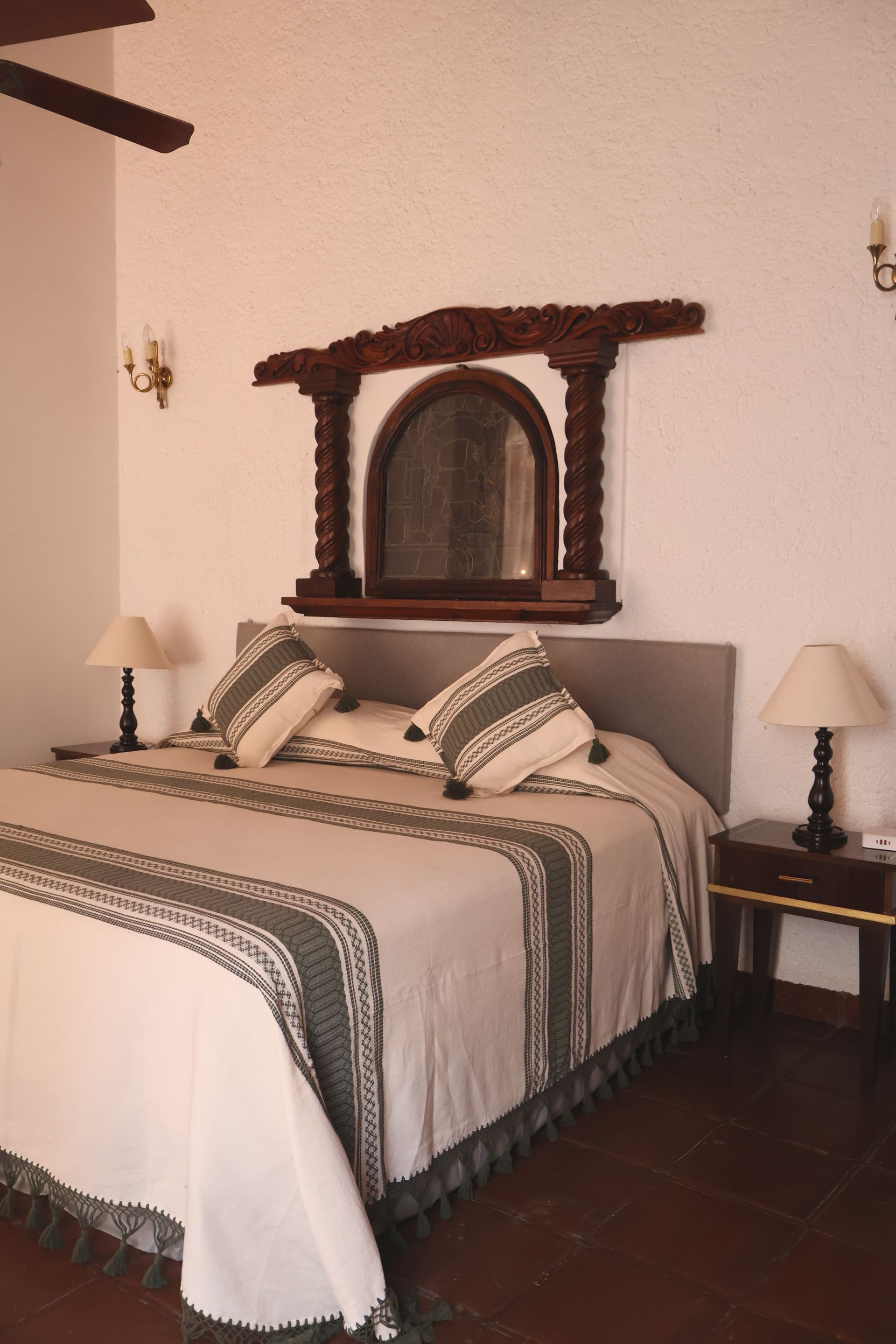 Dormitorio con cama, espejo y dos mesitas de noche. Paredes blancas y molduras de madera oscura.