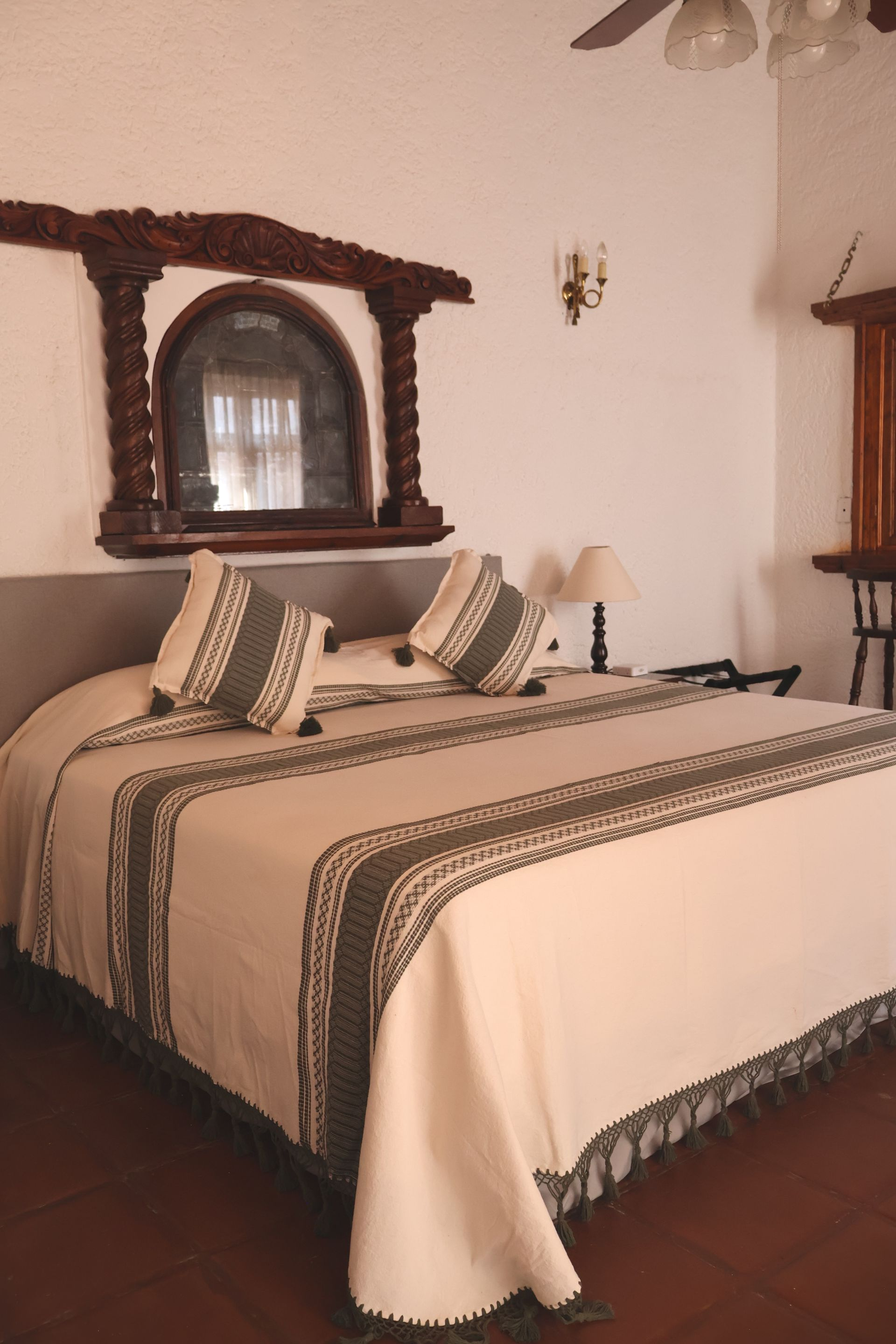Dormitorio con cama tamaño king, molduras decorativas de madera en el espejo, colores neutros y ropa de cama estampada.