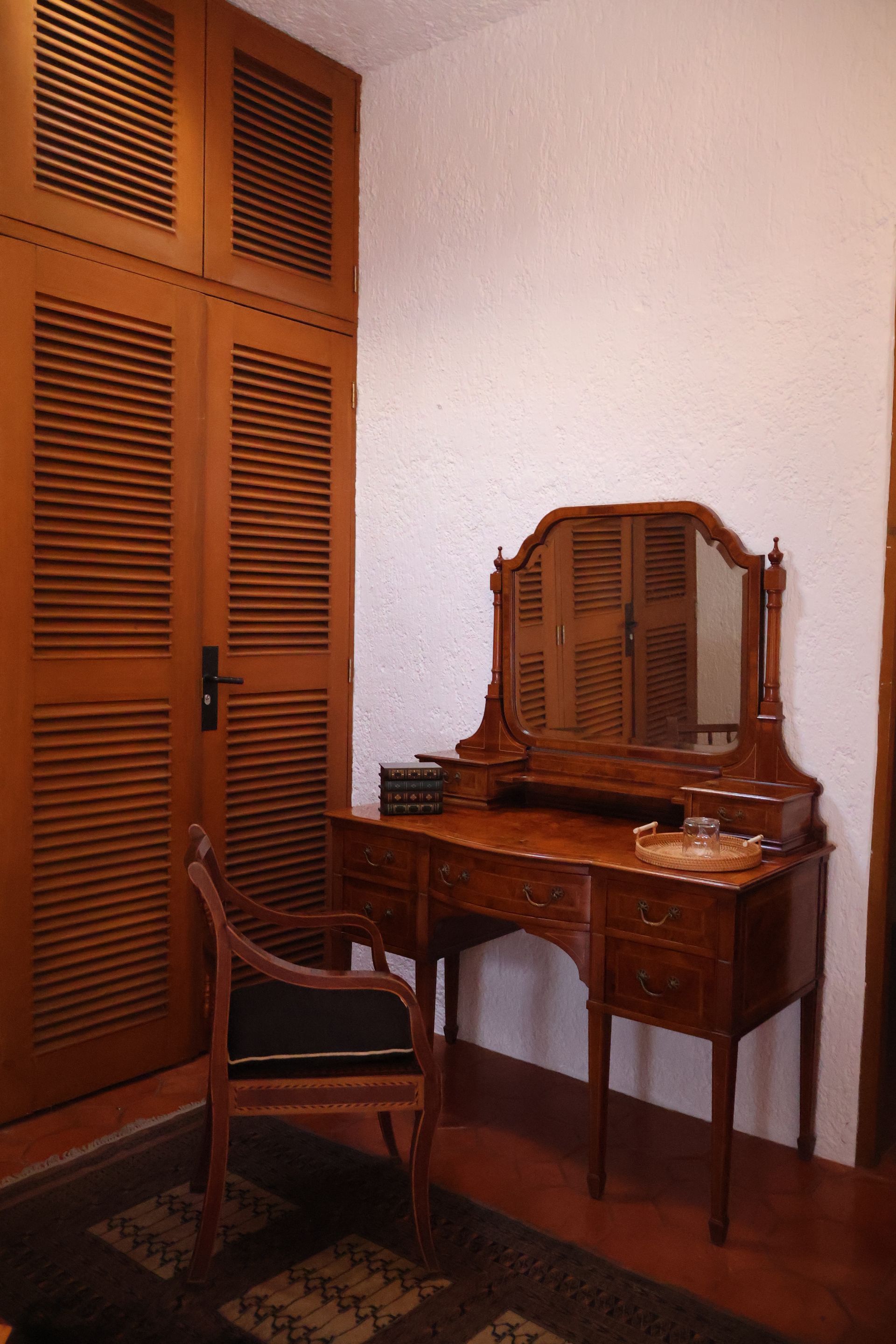Tocador de madera con espejo y silla junto a un amplio armario en una habitación con suelo de madera.